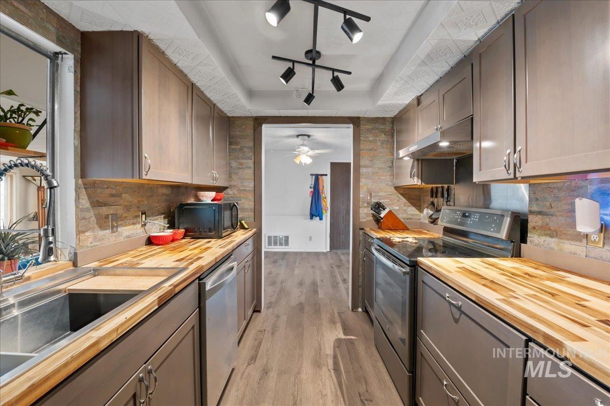 Kitchen with wood counters, appliances with stainless steel finishes, a raised ceiling, decorative backsplash, and light wood-style floors