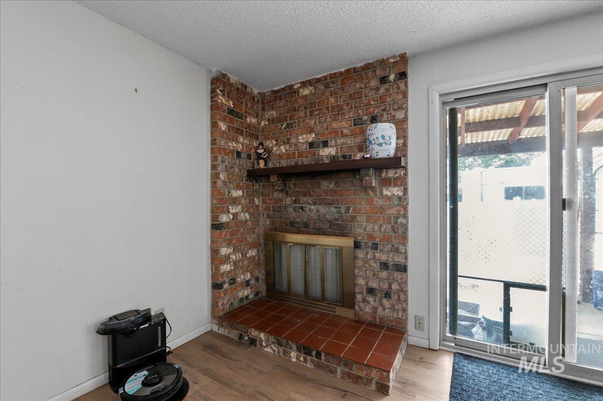 Unfurnished living room featuring wood finished floors, a textured ceiling, and a brick fireplace
