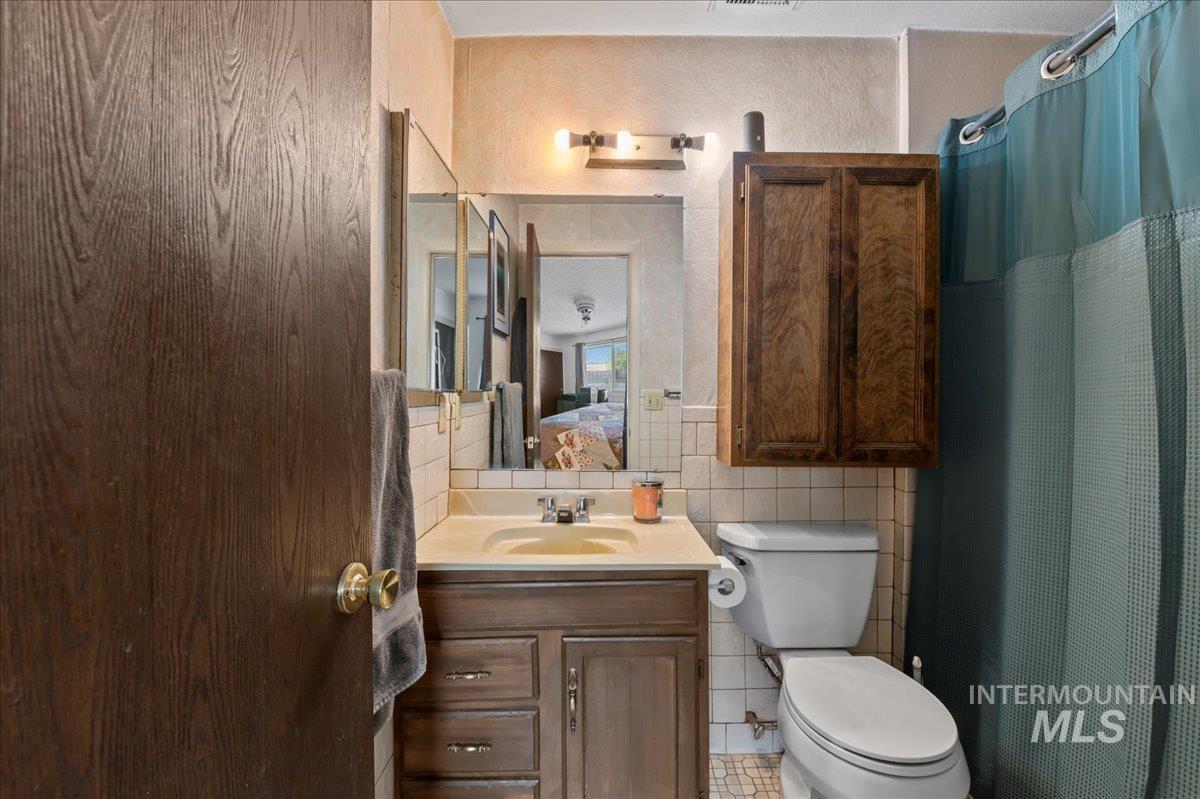 Ensuite bathroom featuring vanity, a shower with shower curtain, tile walls, a textured wall, and decorative backsplash