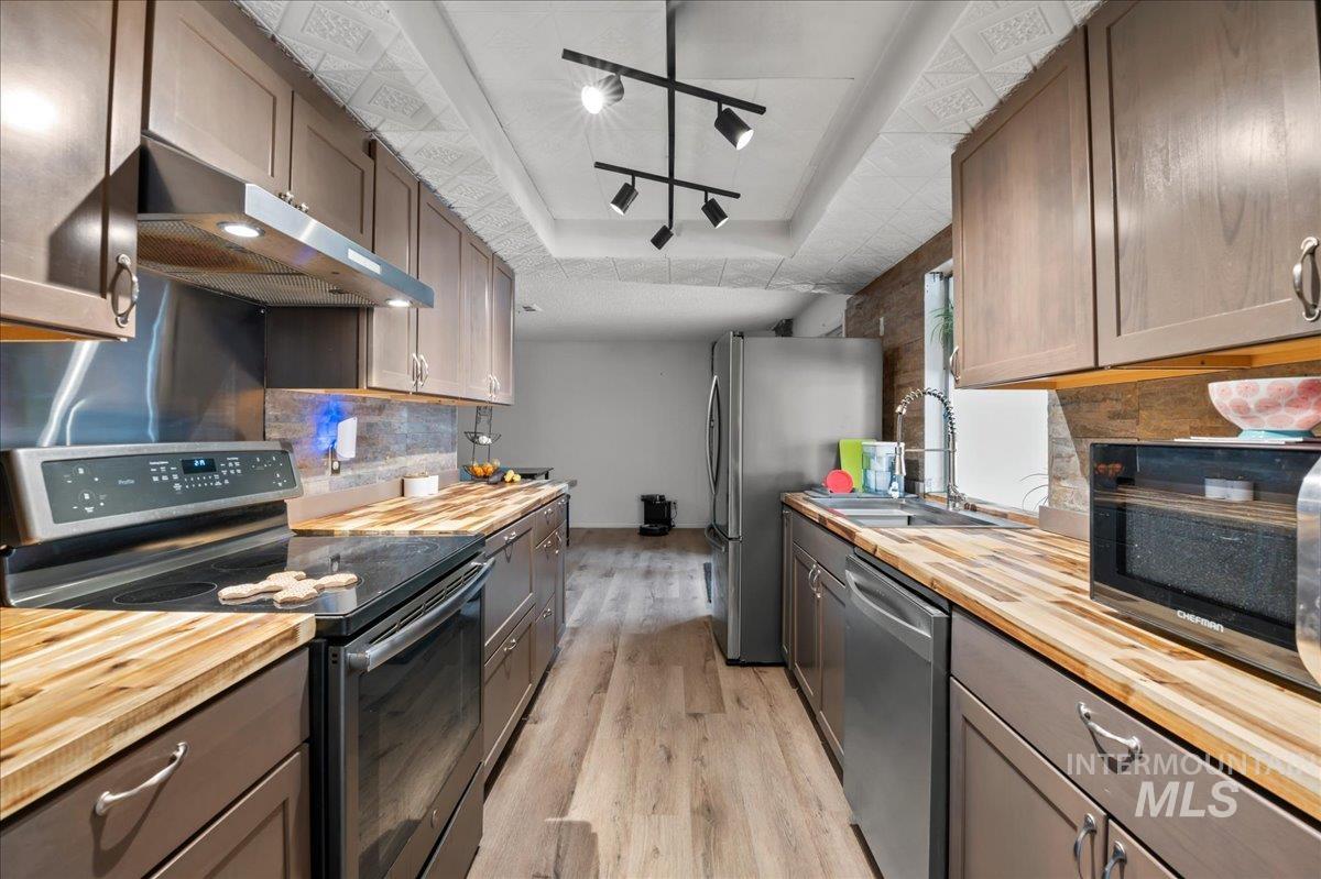 Kitchen featuring appliances with stainless steel finishes, wooden counters, tasteful backsplash, and under cabinet range hood