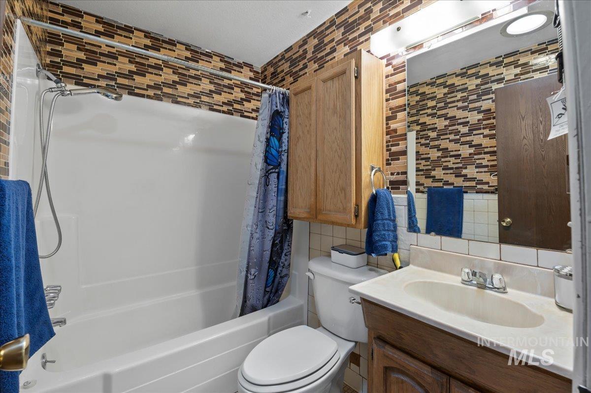 Full bathroom with shower / bath combo, decorative backsplash, vanity, and tile walls