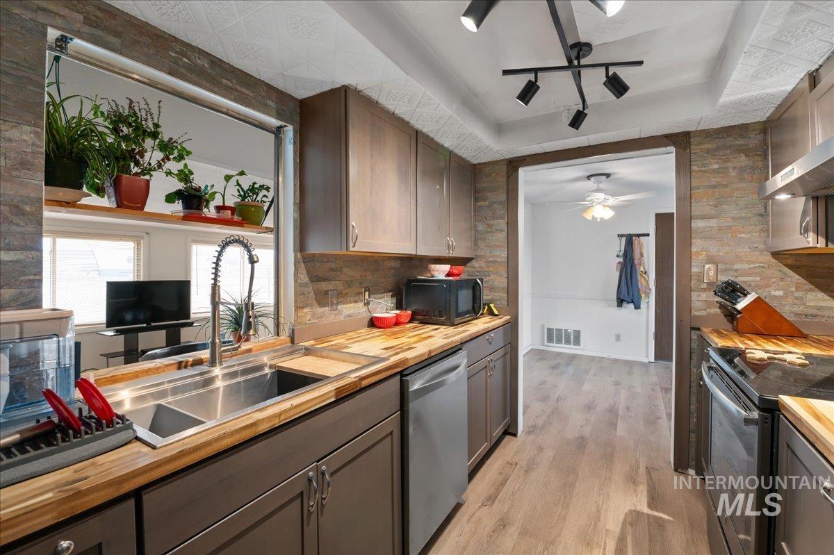 Kitchen with butcher block countertops, a raised ceiling, light wood finished floors, dishwasher, and electric stove