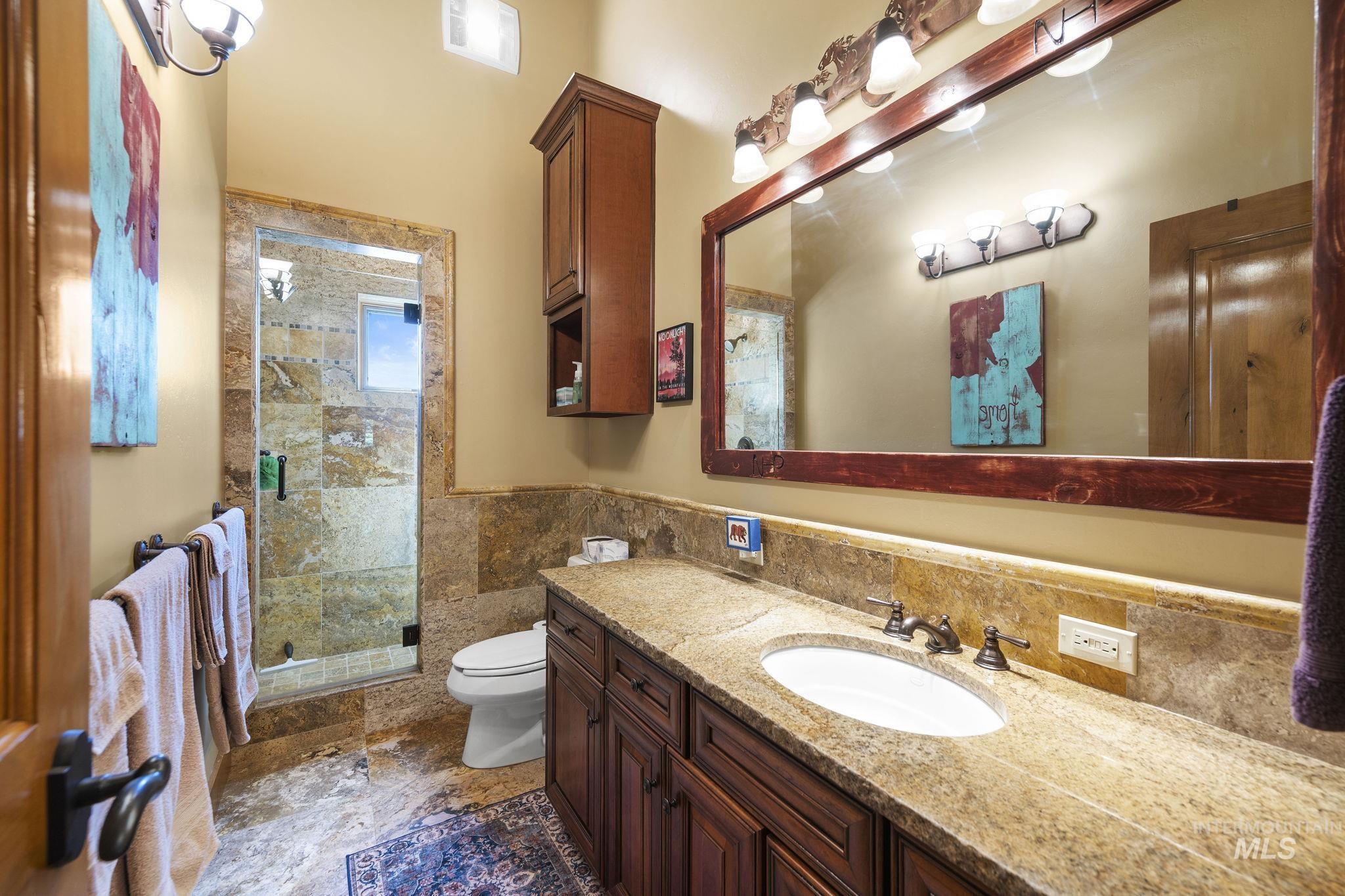 Full bath featuring vanity, a stall shower, tile walls, and wainscoting