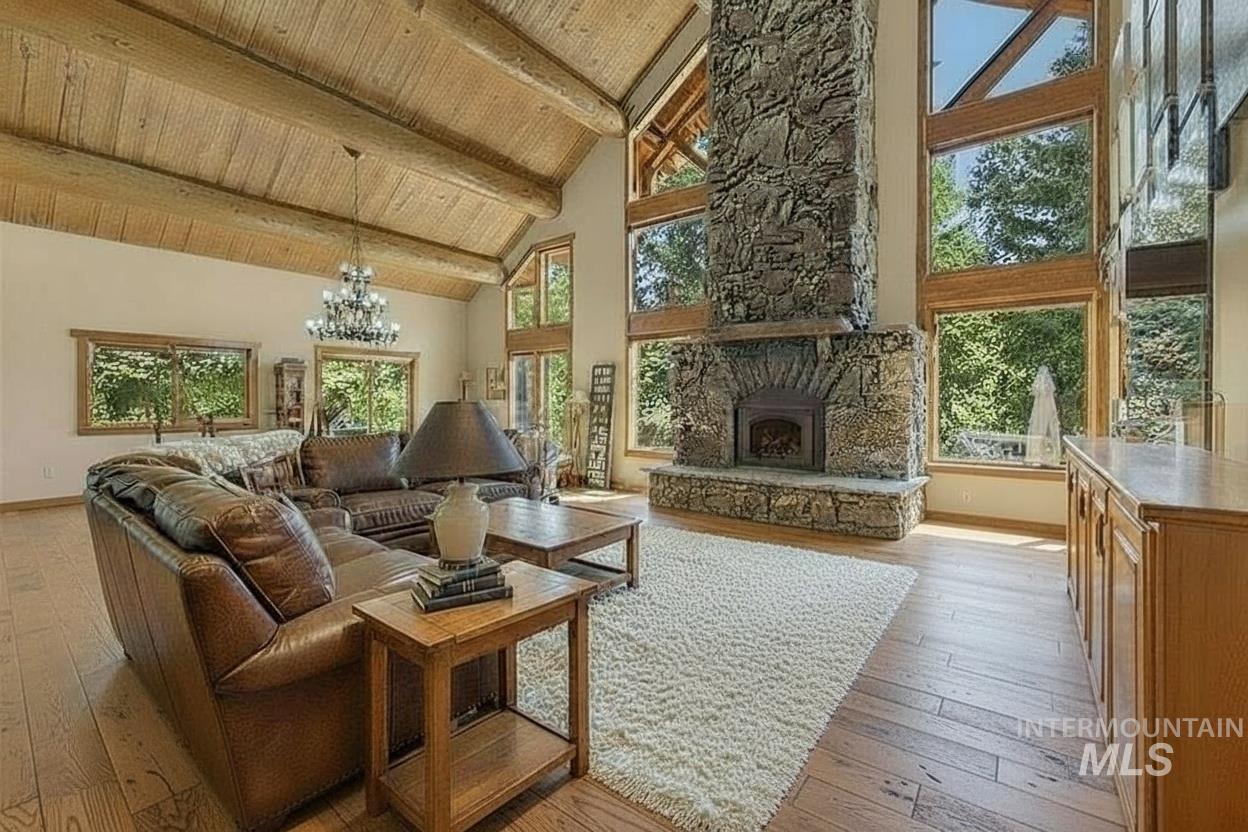 Living area featuring high vaulted ceiling, light wood-style floors, a stone fireplace, healthy amount of natural light, and a chandelier