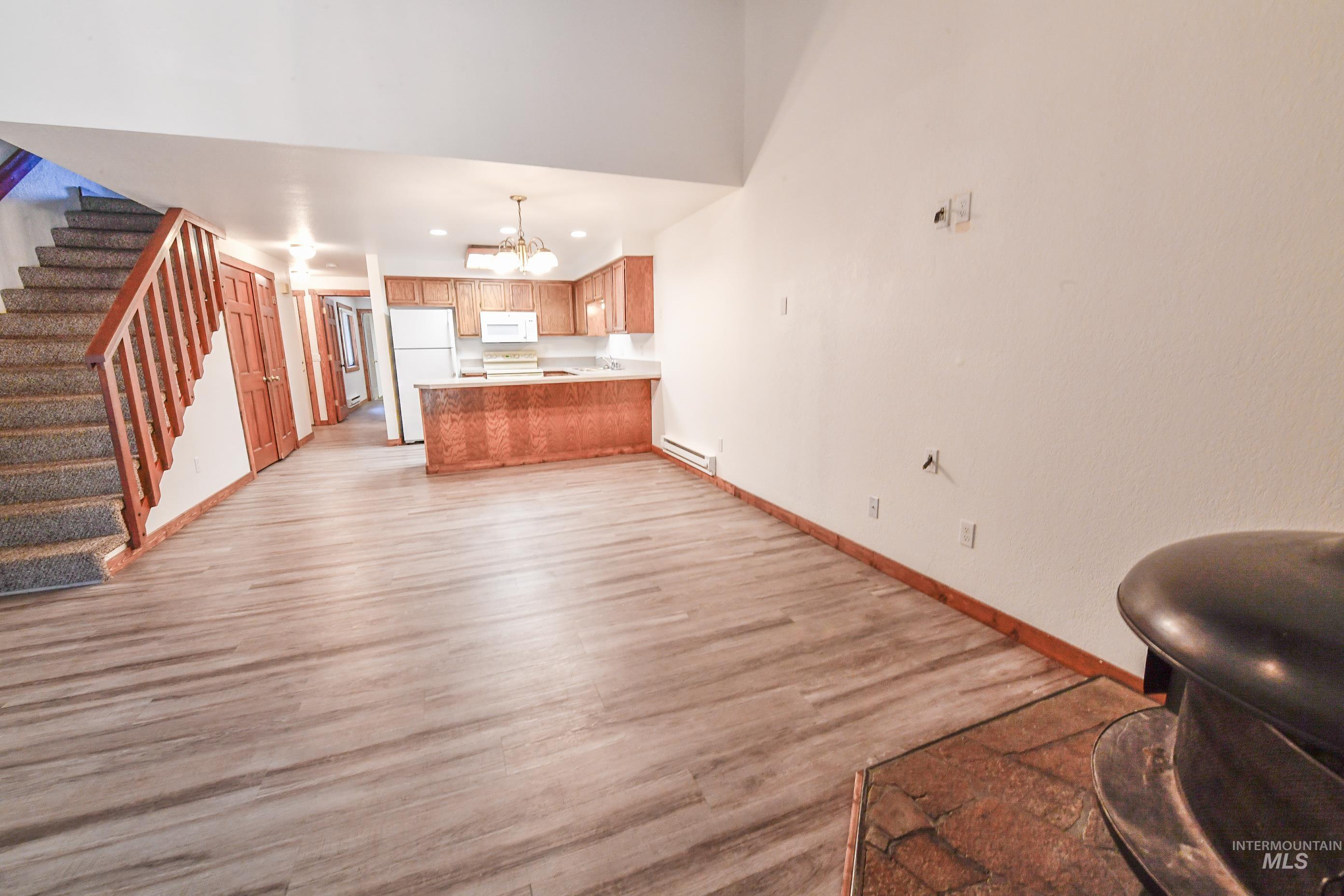 Kitchen with white appliances, a peninsula, a chandelier, open floor plan, and light wood-style flooring