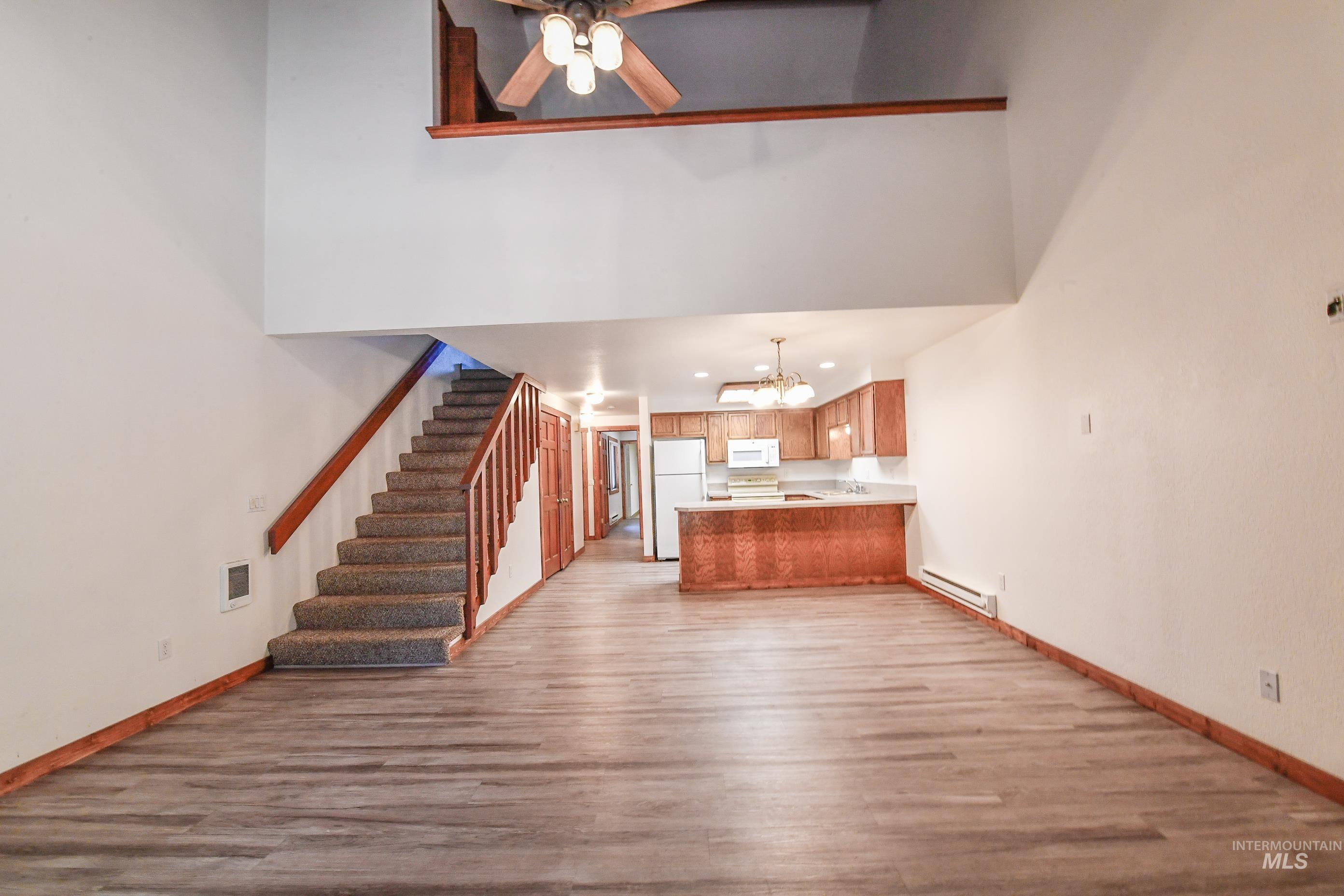 Unfurnished living room featuring light wood finished floors, a chandelier, stairs, a ceiling fan, and a high ceiling