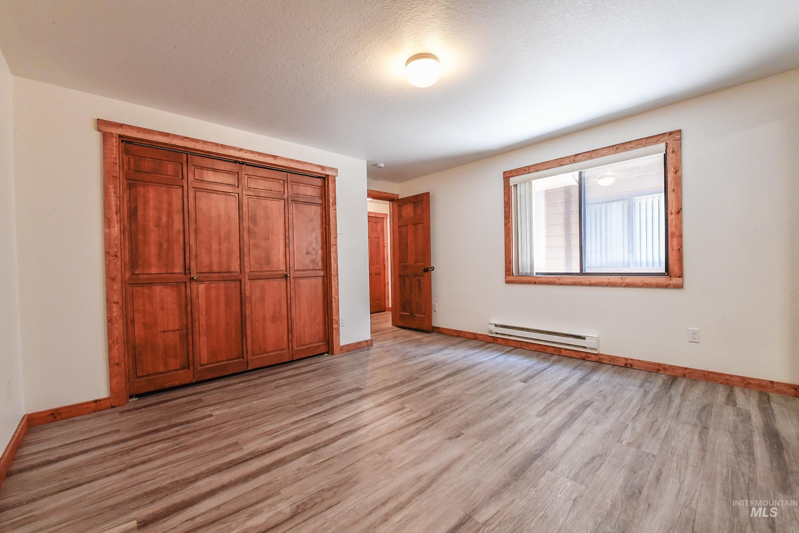 Unfurnished bedroom featuring baseboard heating, light wood-type flooring, and a closet