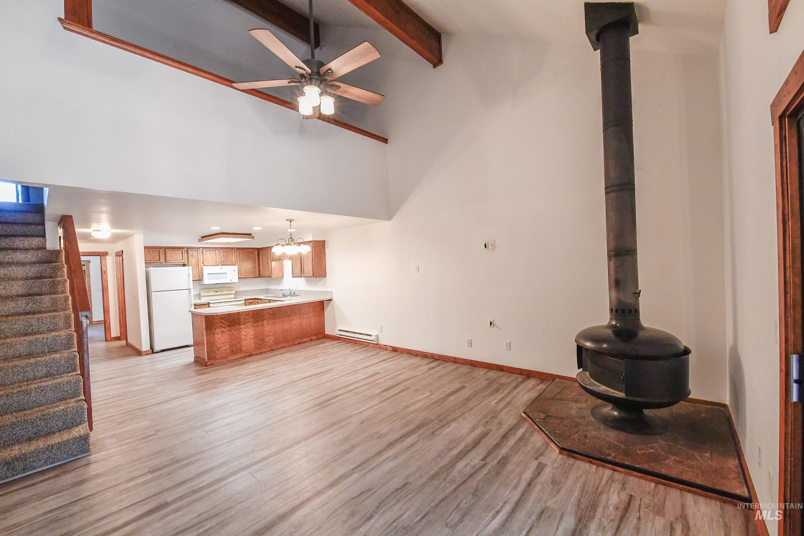 Unfurnished living room featuring light wood-style floors, a baseboard heating unit, stairway, beamed ceiling, and a ceiling fan