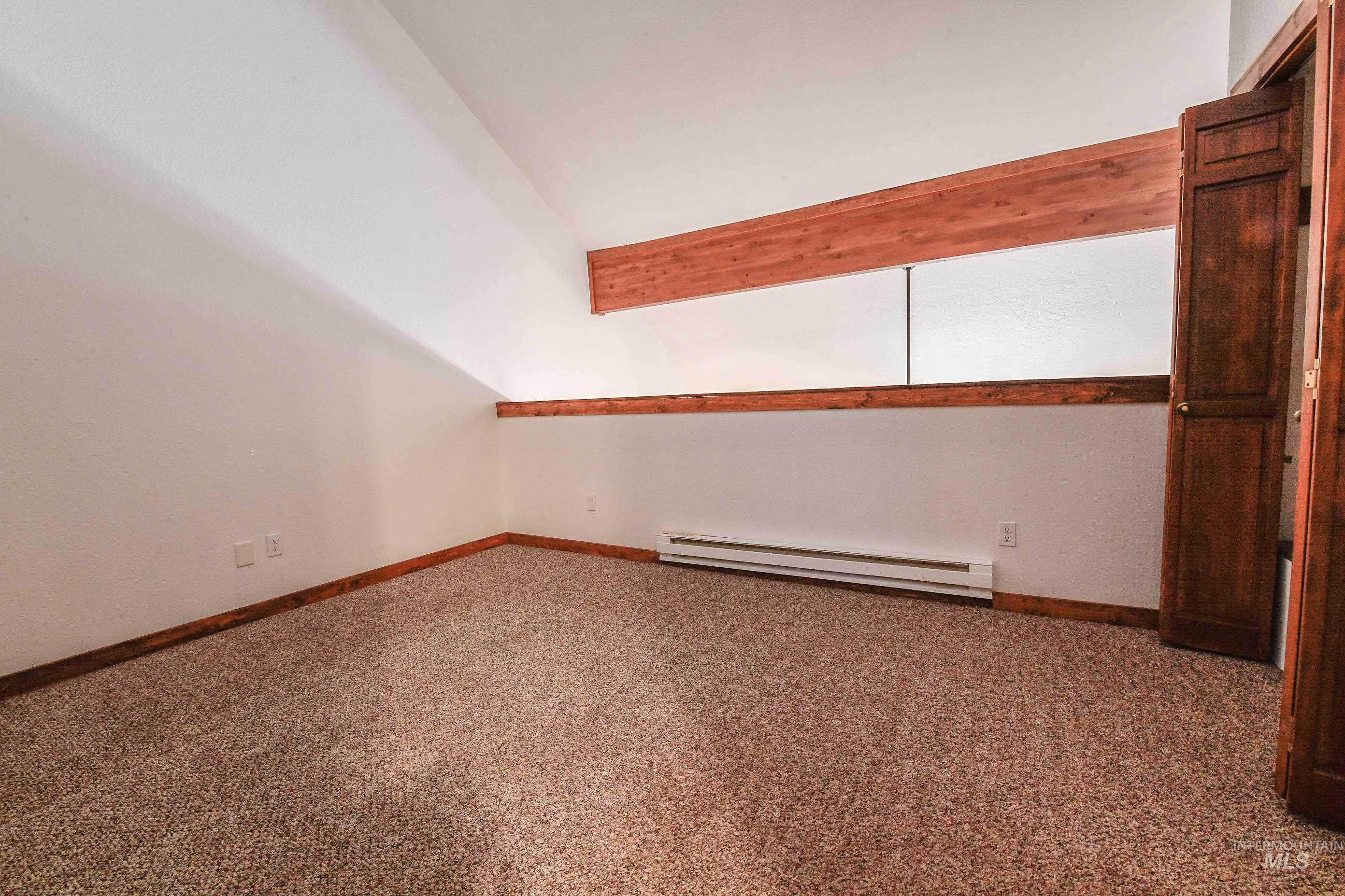 Empty room featuring baseboard heating, lofted ceiling, and carpet floors
