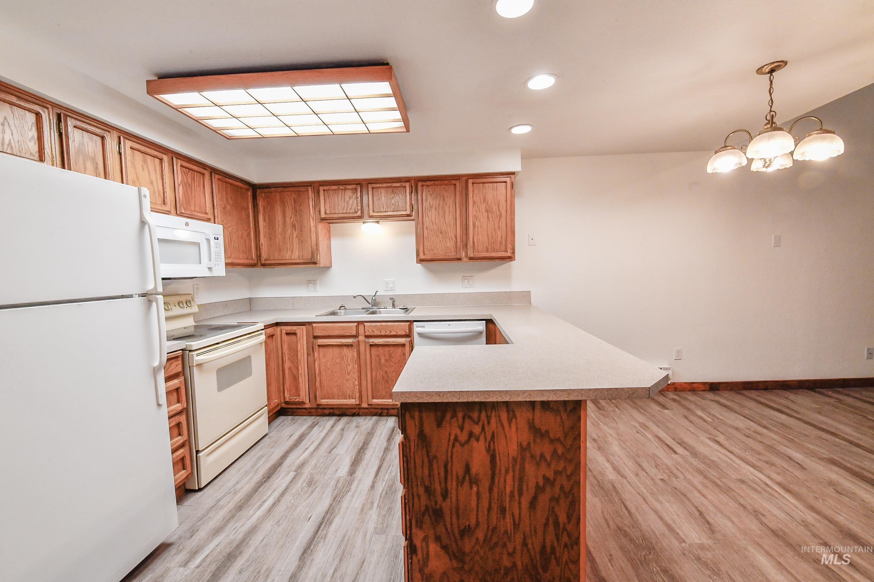 Kitchen with white appliances, a peninsula, light wood-style floors, light countertops, and recessed lighting