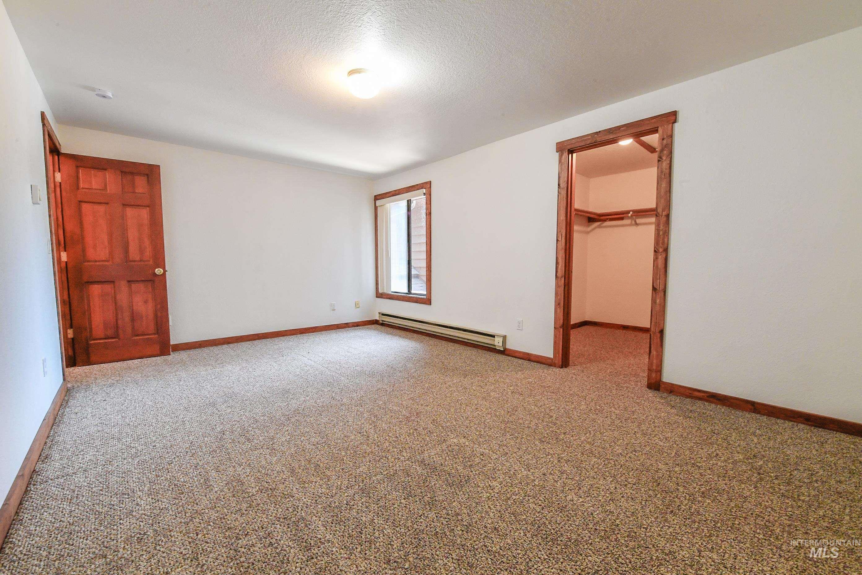 Carpeted empty room featuring a baseboard heating unit and baseboards