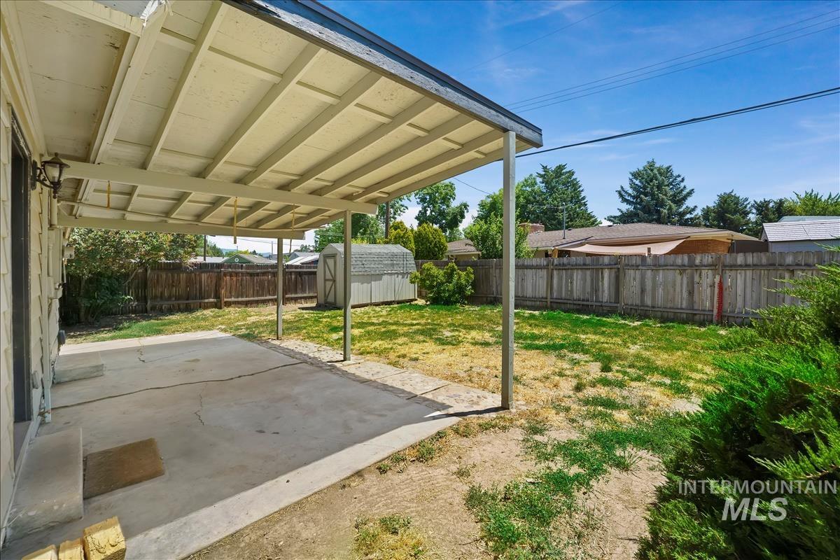 Covered concrete patio extending into a fenced backyard with a storage shed