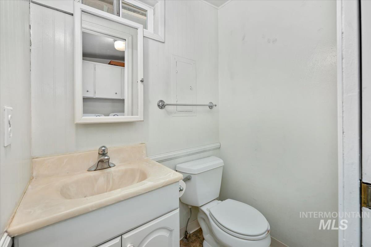 Compact bathroom featuring a corner vanity with integrated sink, wall-mounted mirror cabinet, toilet, and white paneled walls