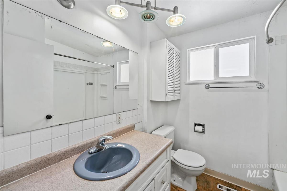 Bathroom featuring a vanity with a countertop and undermount sink, a large wall-mounted mirror, white square tile backsplash, and a window