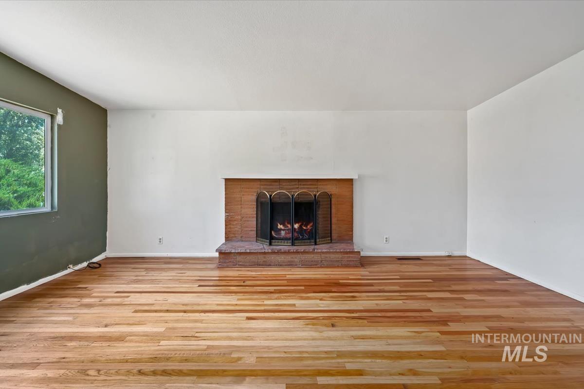 Spacious room featuring wood-finish flooring, a brick fireplace with hearth, and a window