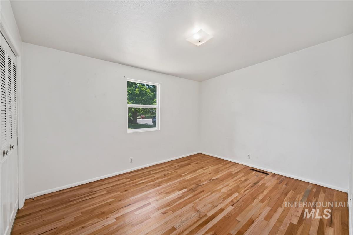 Room featuring wood flooring, neutral wall tones, a single window, a ceiling-mounted light fixture, and bifold louvered closet doors