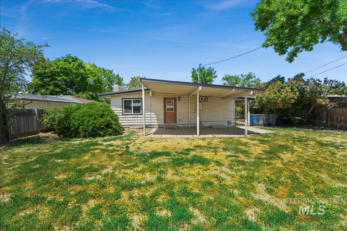 Expansive backyard featuring a covered patio, a large grass area, mature perimeter fencing, and established shrubbery