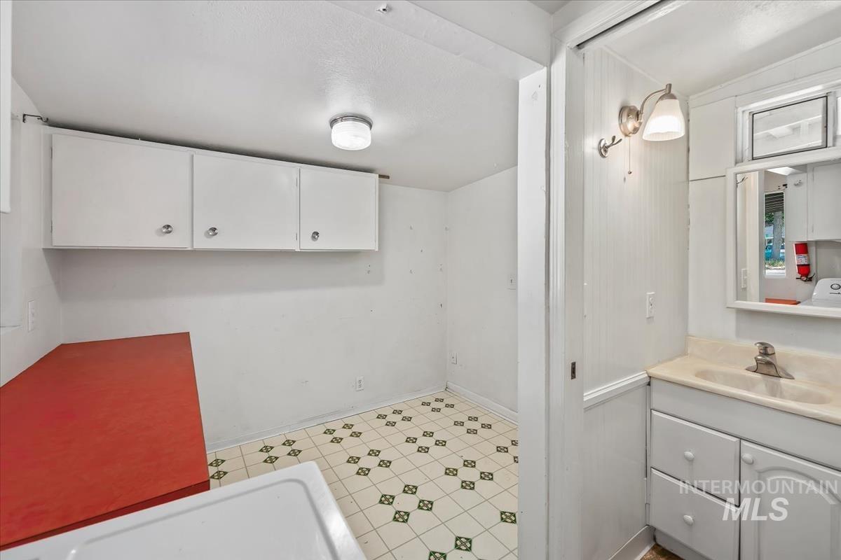 Compact utility area featuring white cabinetry, a red countertop, and patterned tile flooring