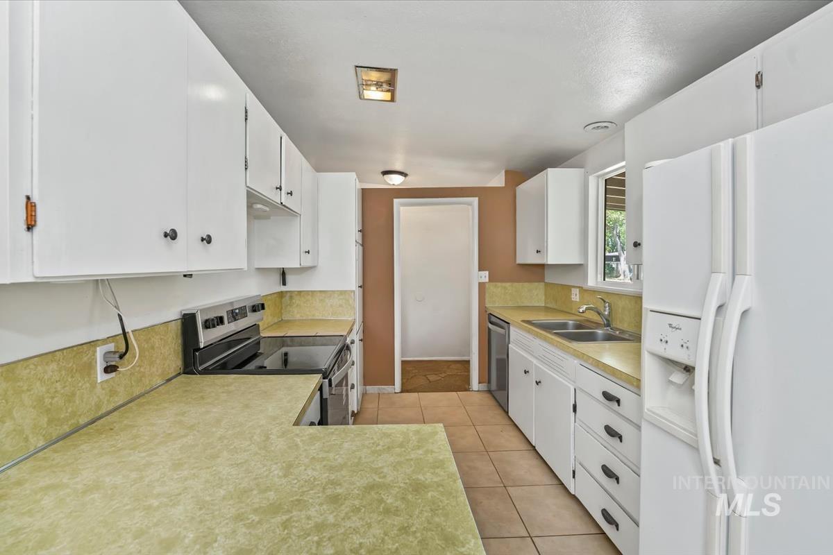 Galley kitchen featuring ample white cabinetry, a dual basin stainless steel sink, a stainless steel electric range, and tile flooring