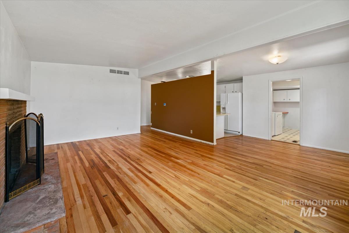 Spacious interior featuring wood-finish flooring, a brick fireplace with hearth, and white walls
