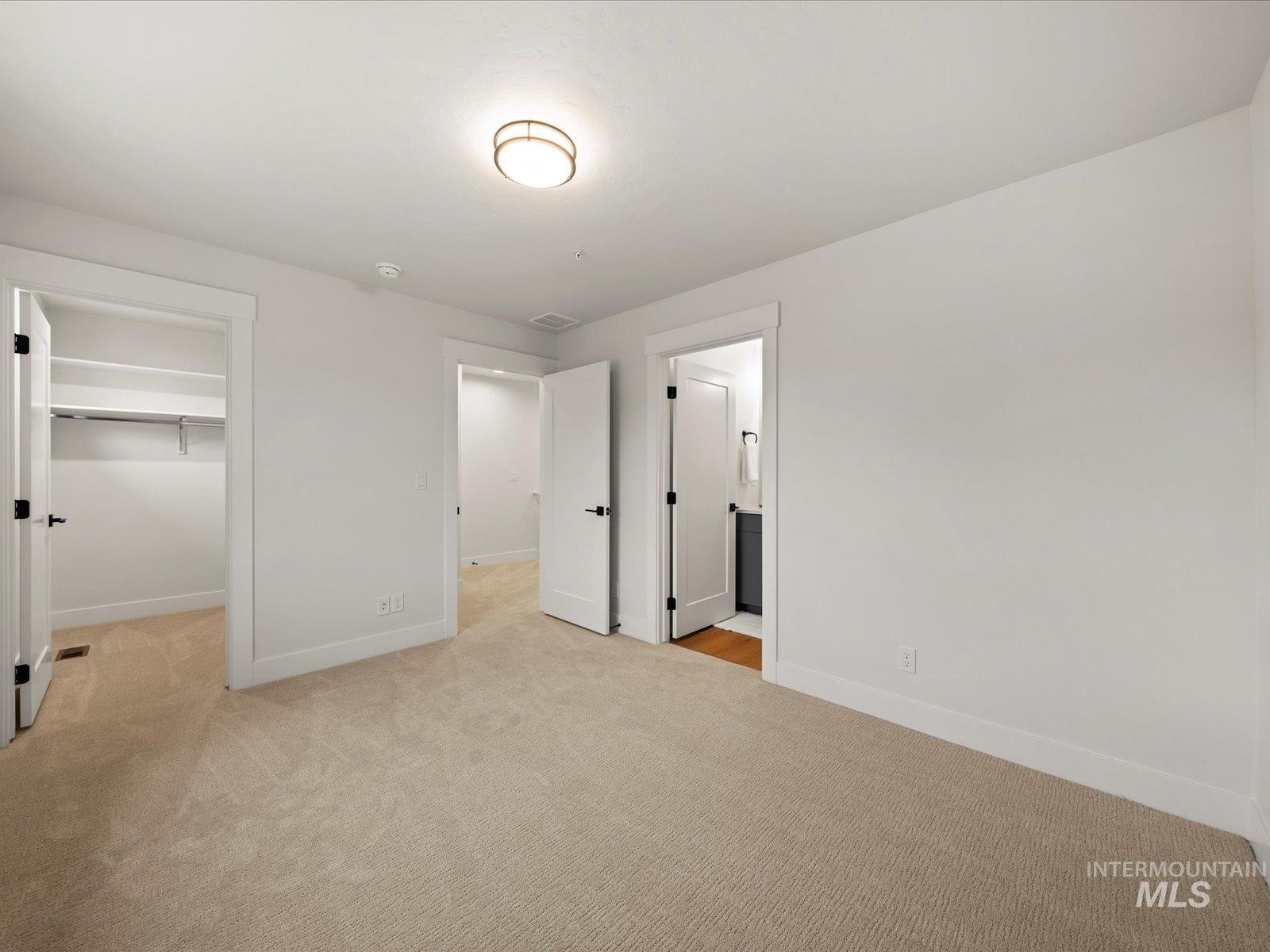 Unfurnished bedroom featuring a walk in closet, light colored carpet, and ensuite bathroom