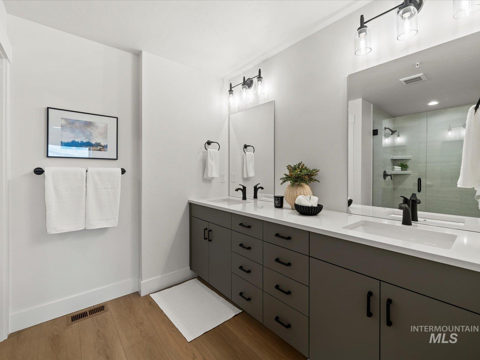 Bathroom featuring double vanity, a shower stall, and light wood-style flooring