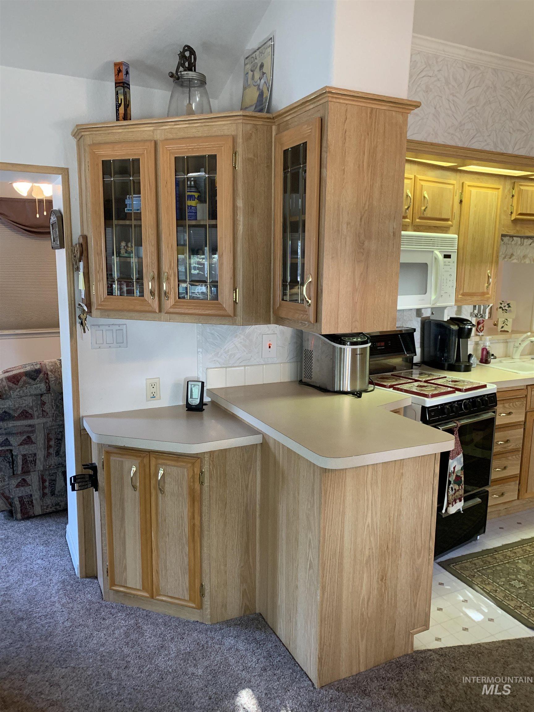 Kitchen with black range oven, light colored carpet, white microwave, light countertops, and glass insert cabinets