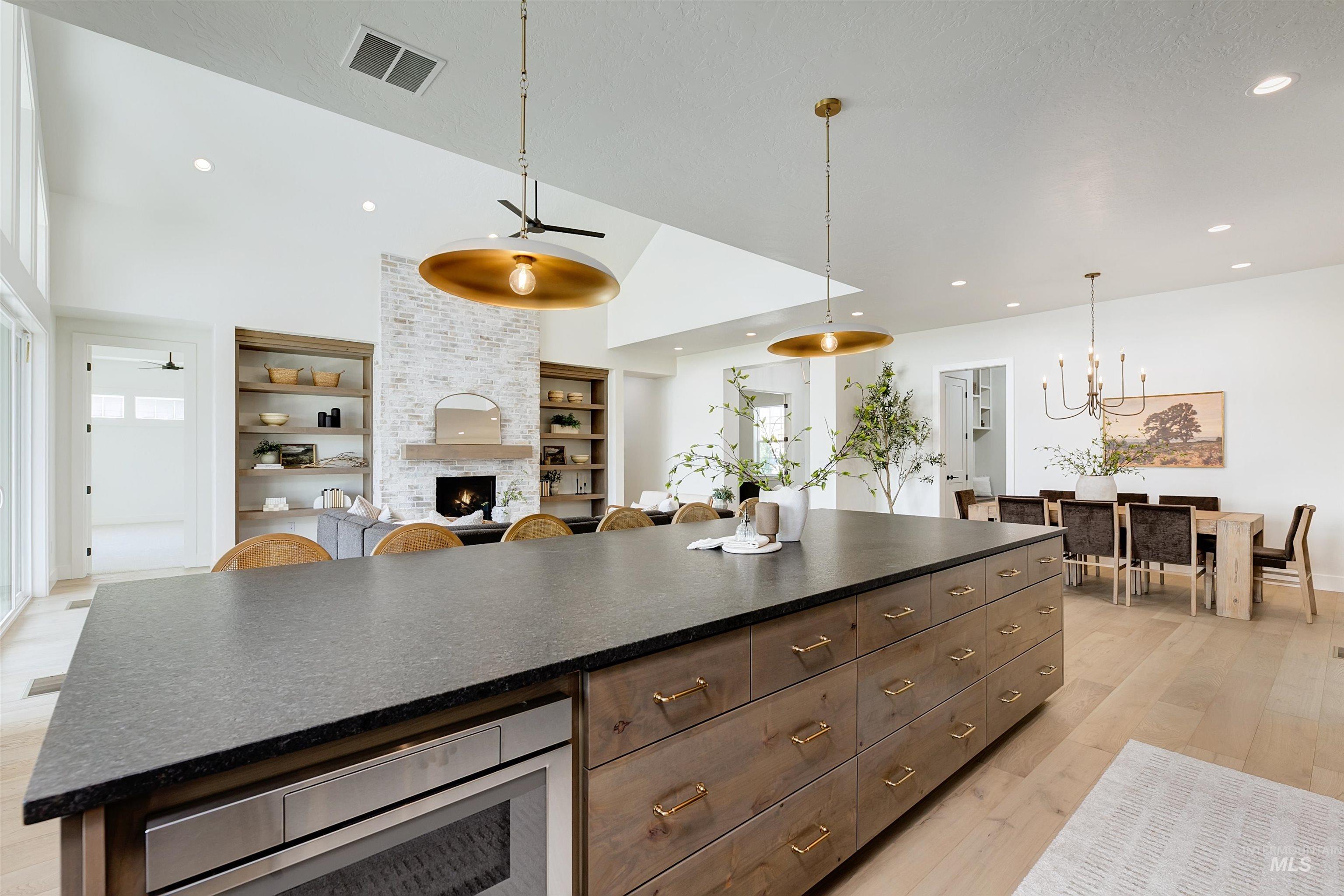 Kitchen featuring dark brown cabinetry, hanging light fixtures, a large fireplace, a ceiling fan, and light wood-style flooring
