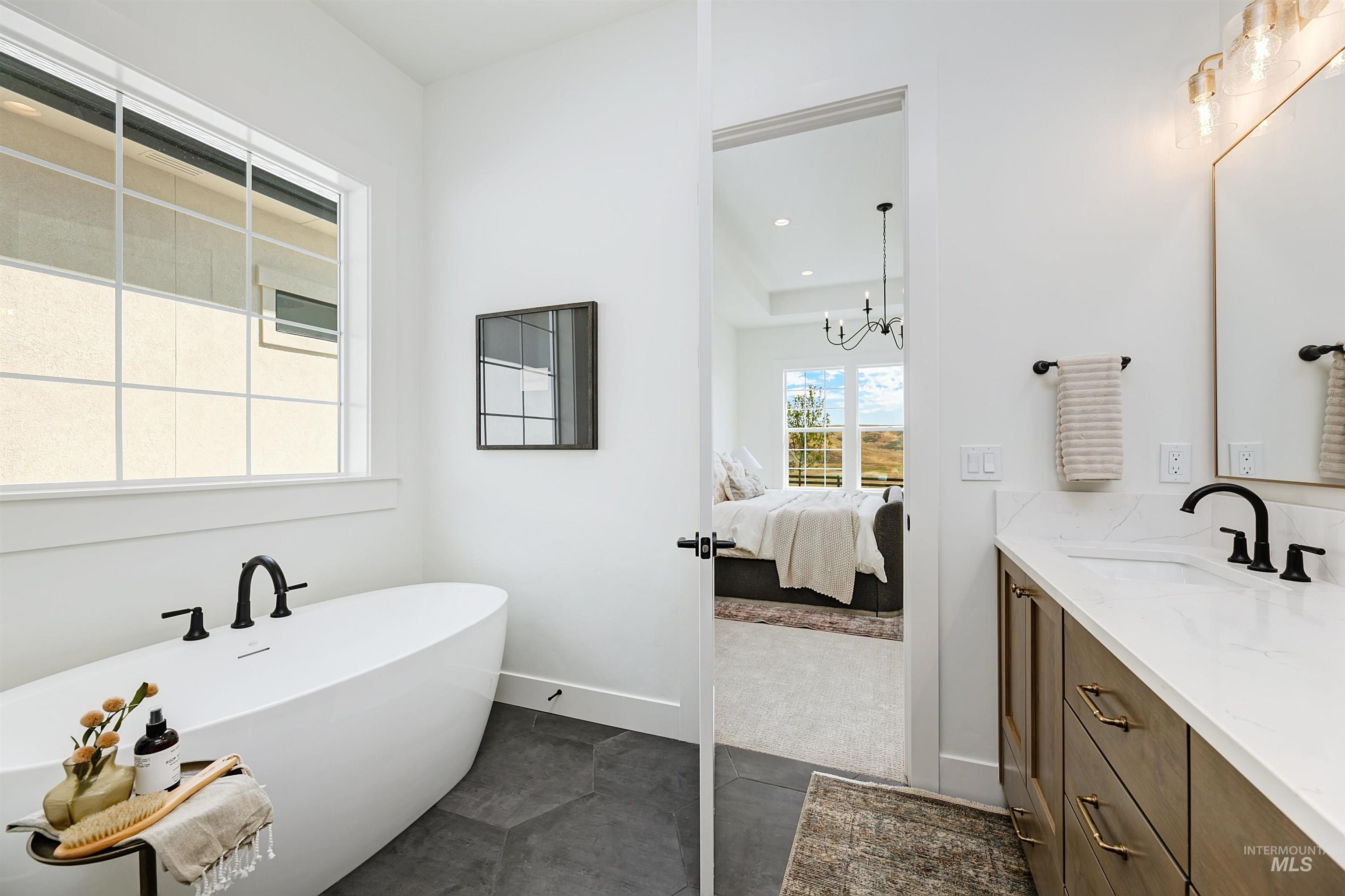 Bathroom featuring double vanity, a freestanding tub, a chandelier, dark tile patterned flooring, and ensuite bath