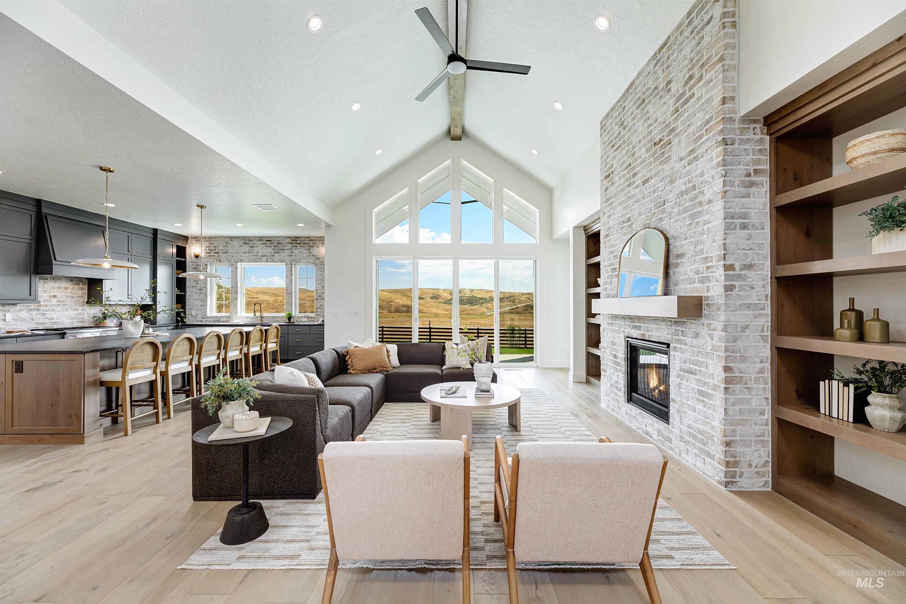 Living room with beamed ceiling, light wood finished floors, high vaulted ceiling, a fireplace, and a ceiling fan