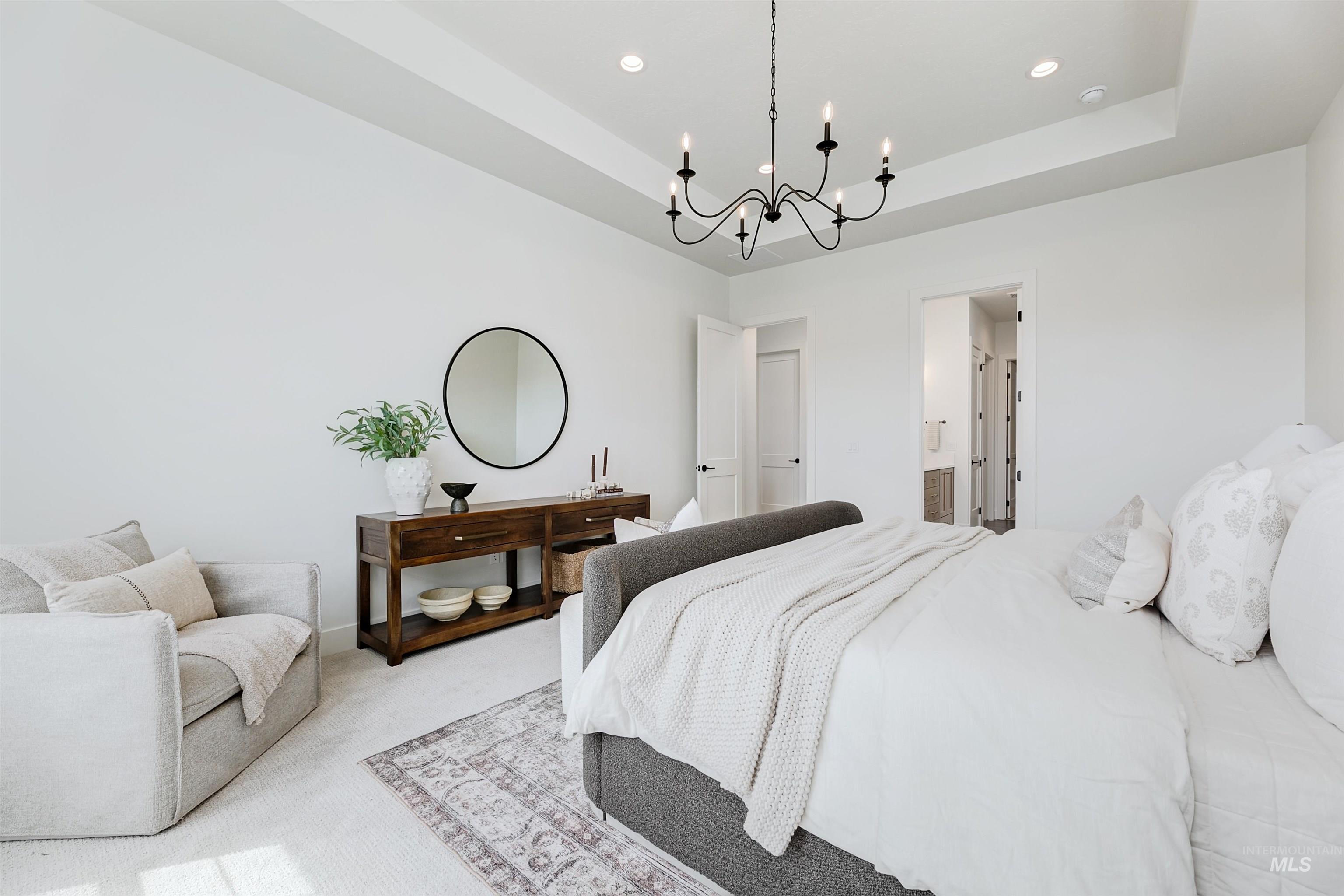 Carpeted bedroom featuring a tray ceiling, a chandelier, recessed lighting, and connected bathroom