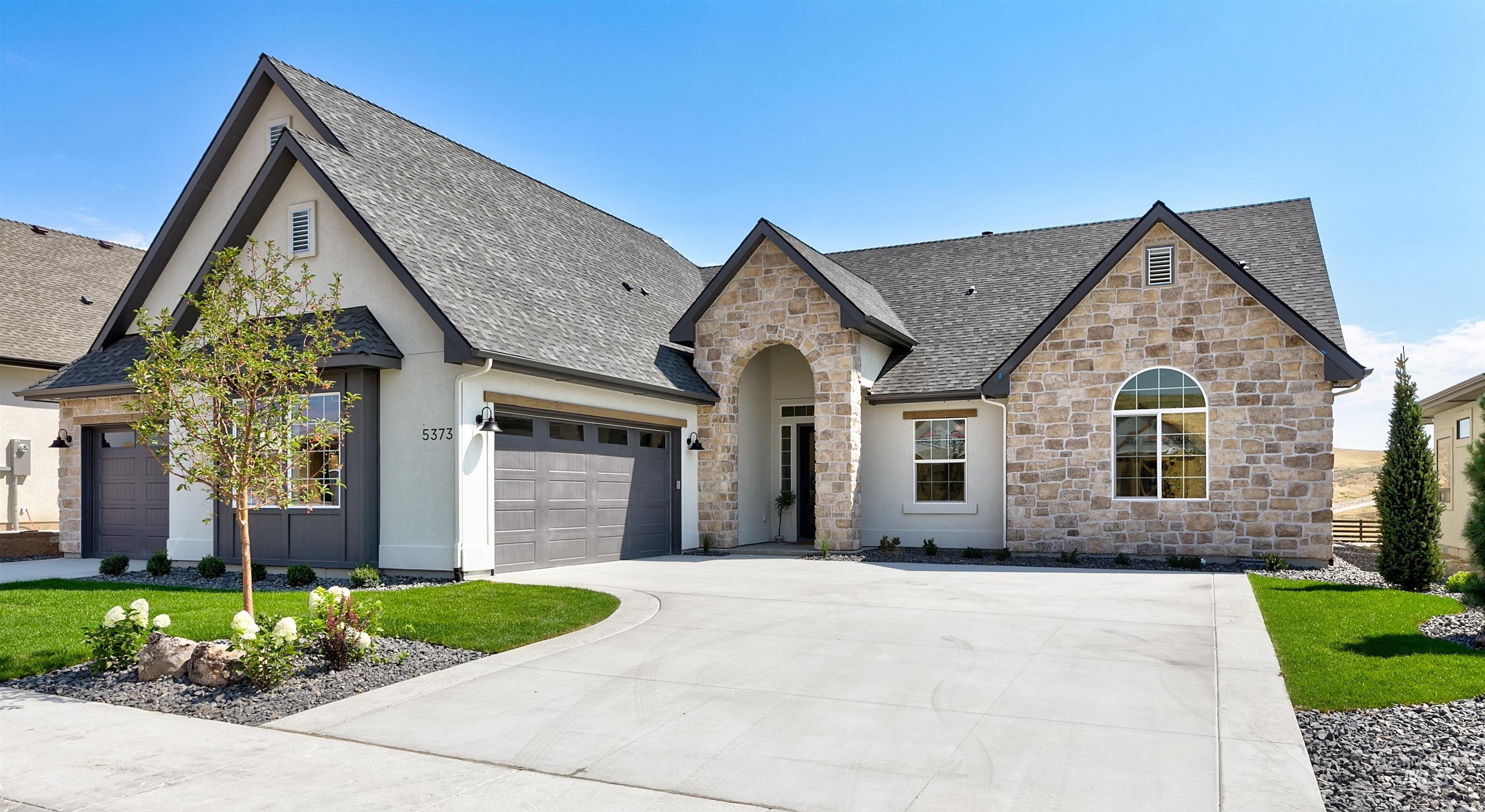 French country home with stone siding, roof with shingles, and concrete driveway
