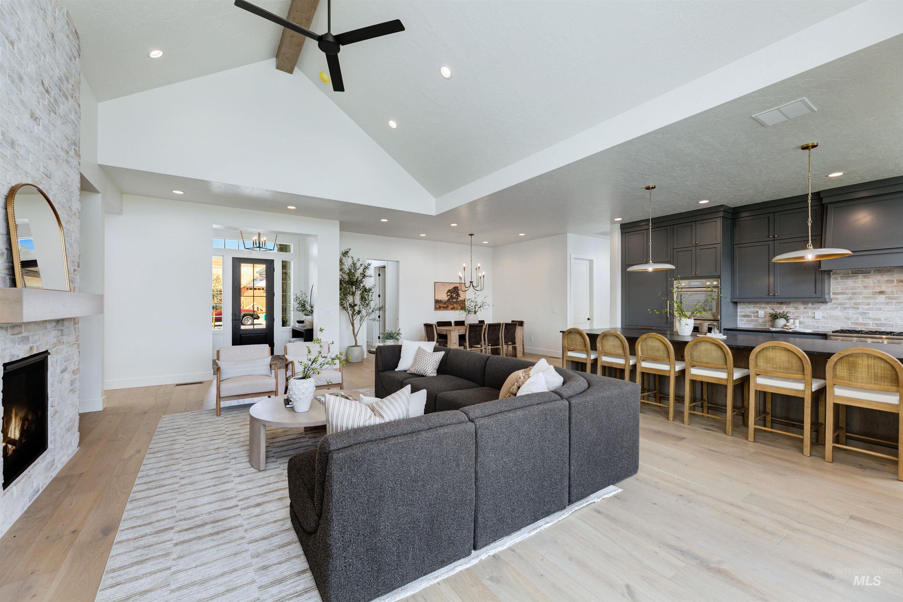 Living area with beamed ceiling, light wood-style flooring, a stone fireplace, high vaulted ceiling, and a ceiling fan