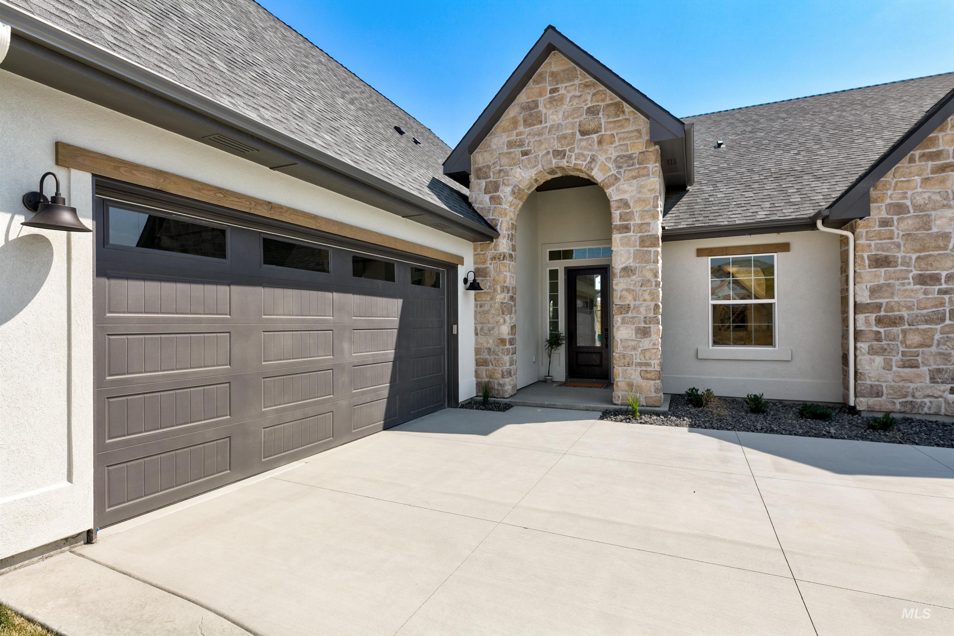 View of front of property featuring a shingled roof, stone siding, driveway, and stucco siding
