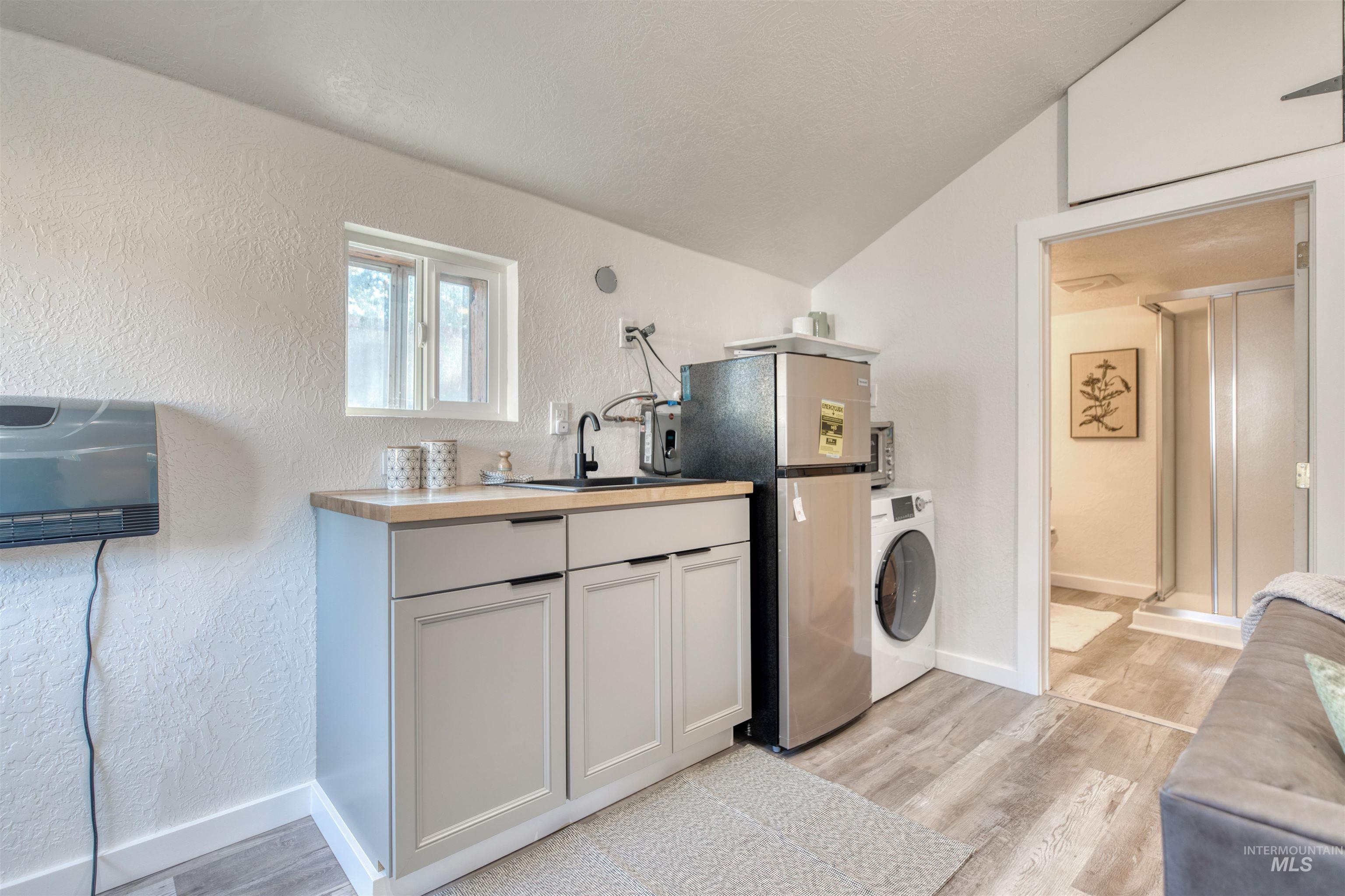 Kitchen featuring a textured wall, light wood-style flooring, freestanding refrigerator, washer / dryer, and vaulted ceiling