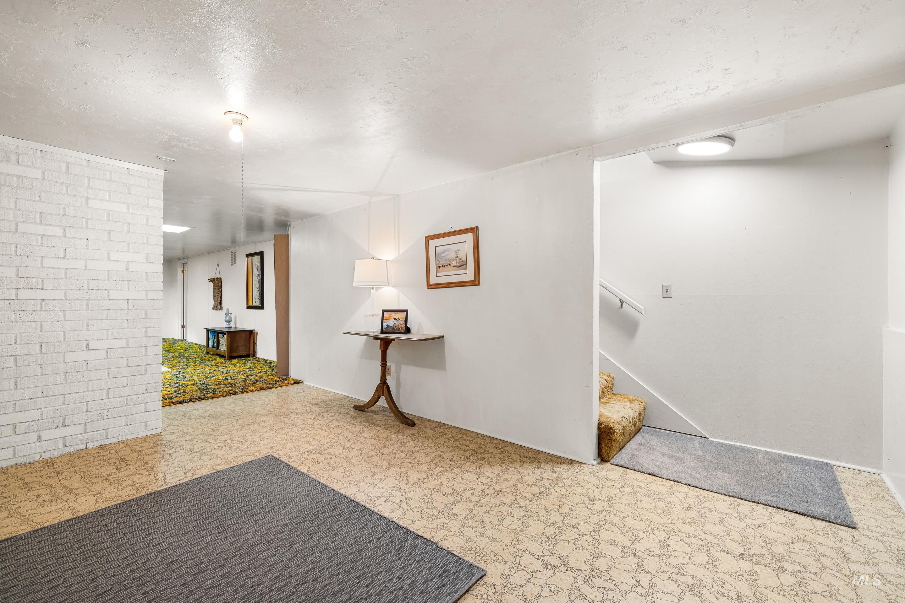 Finished basement with tile patterned floors, a textured ceiling, stairway, and brick wall