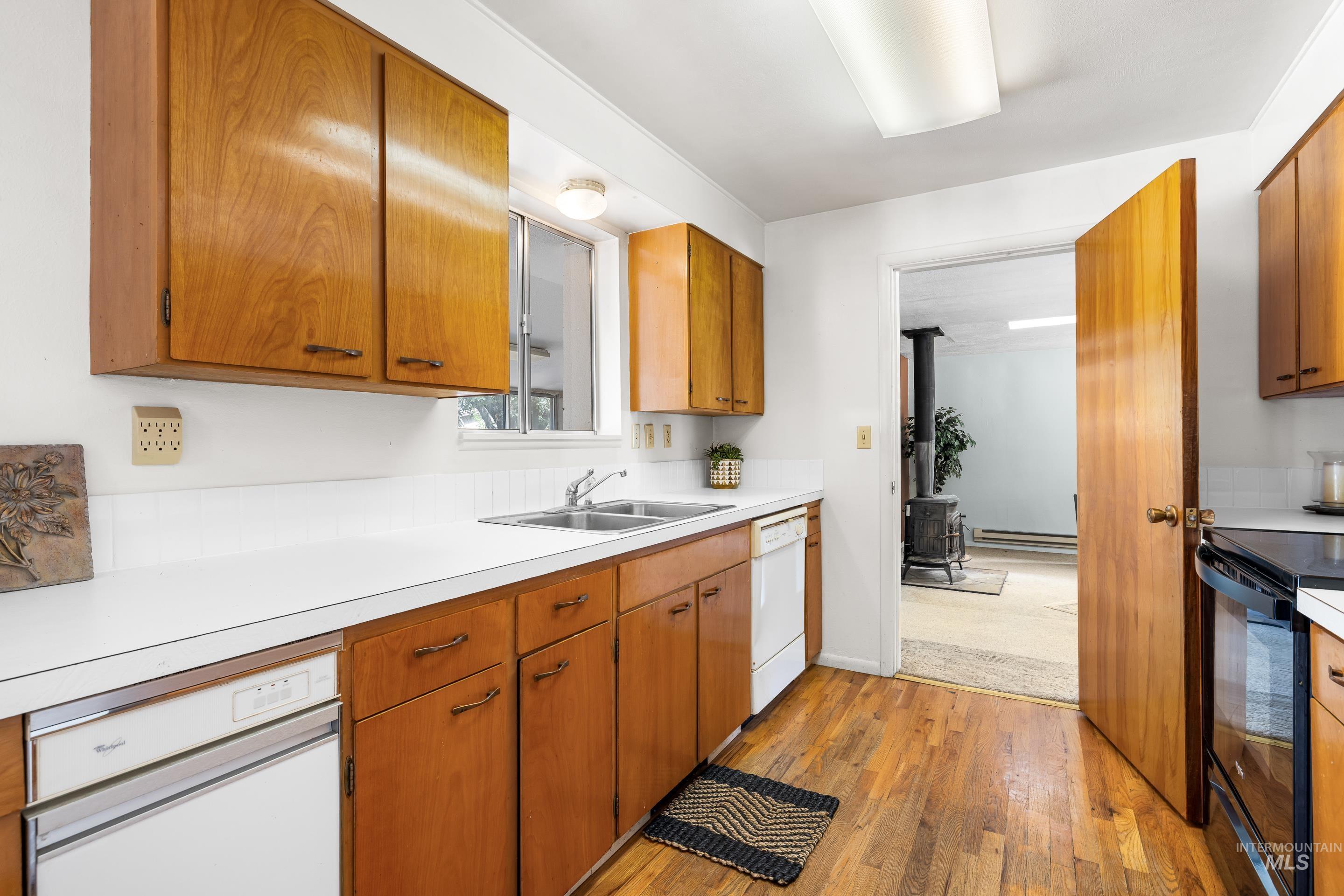Kitchen featuring black range with electric stovetop, brown cabinets, light countertops, light wood finished floors, and dishwasher