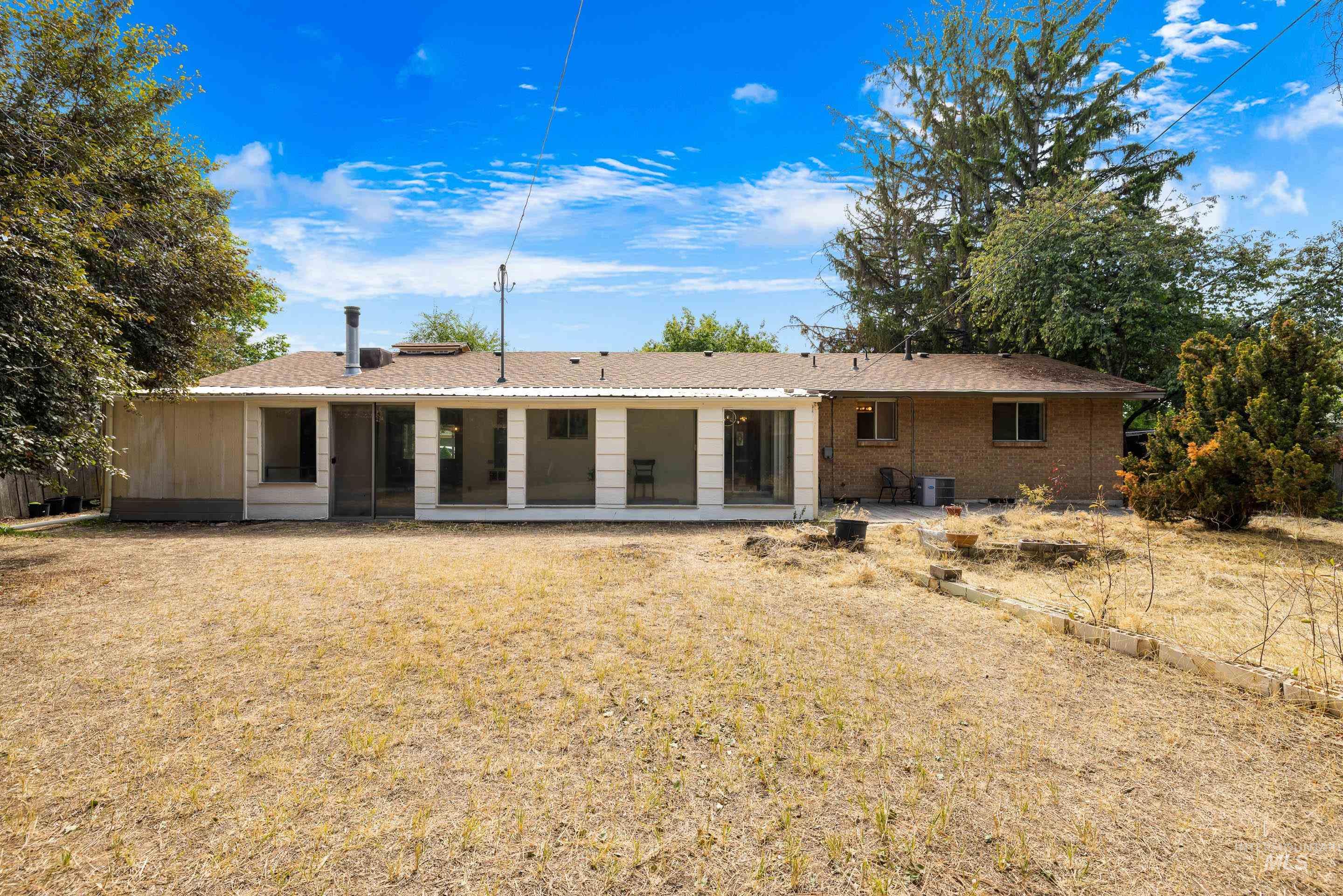 Rear view of property with brick siding, a patio, a lawn, roof with shingles, and a sunroom