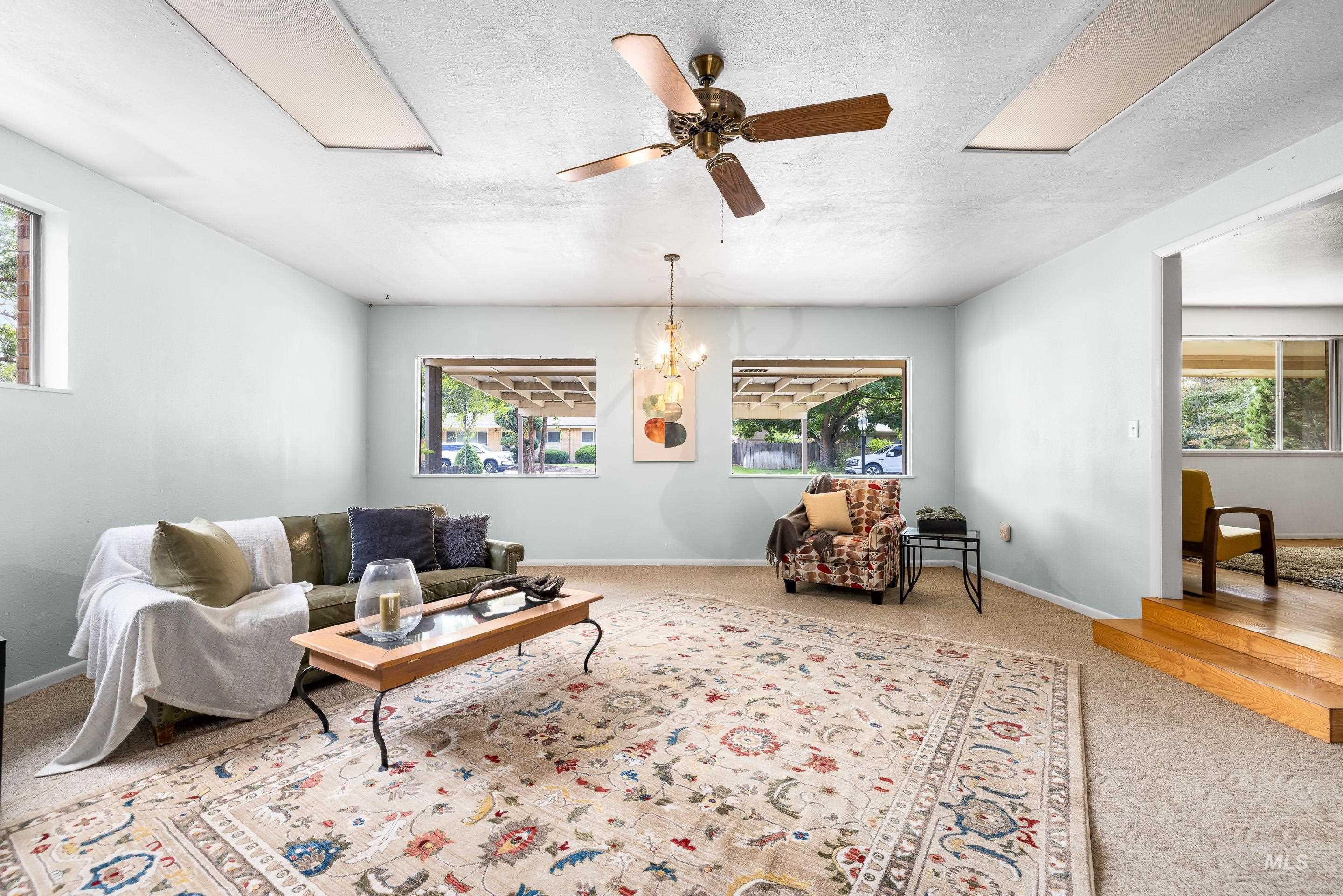 Living area featuring a textured ceiling, carpet flooring, ceiling fan, and a chandelier