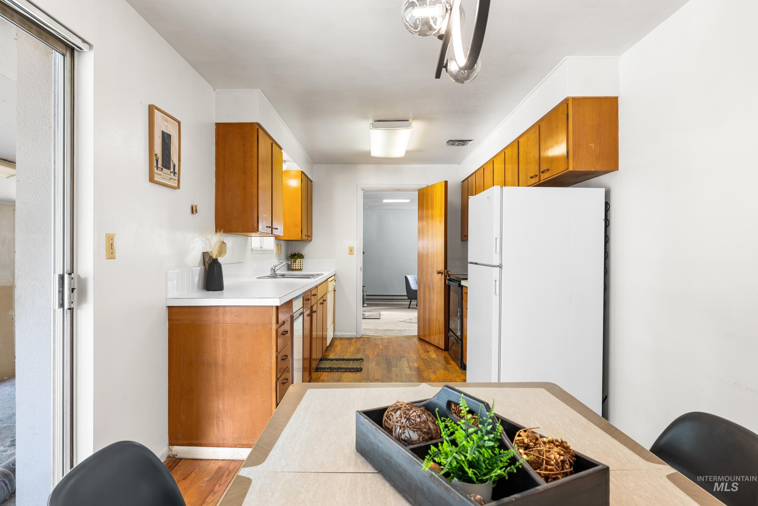Kitchen featuring brown cabinetry, freestanding refrigerator, light wood-style floors, light countertops, and black / electric stove
