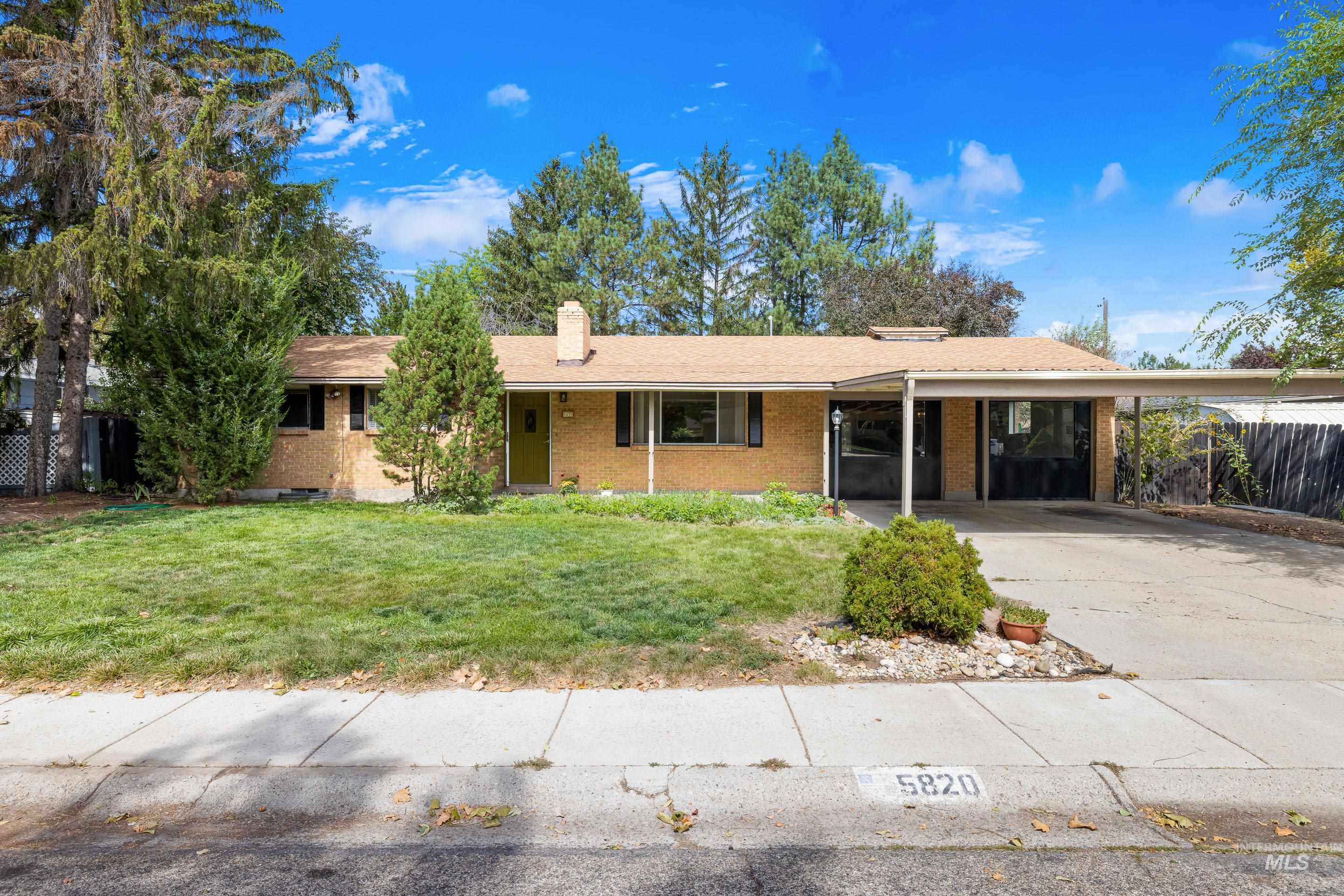 Ranch-style house featuring brick siding, a chimney, driveway, and an attached carport