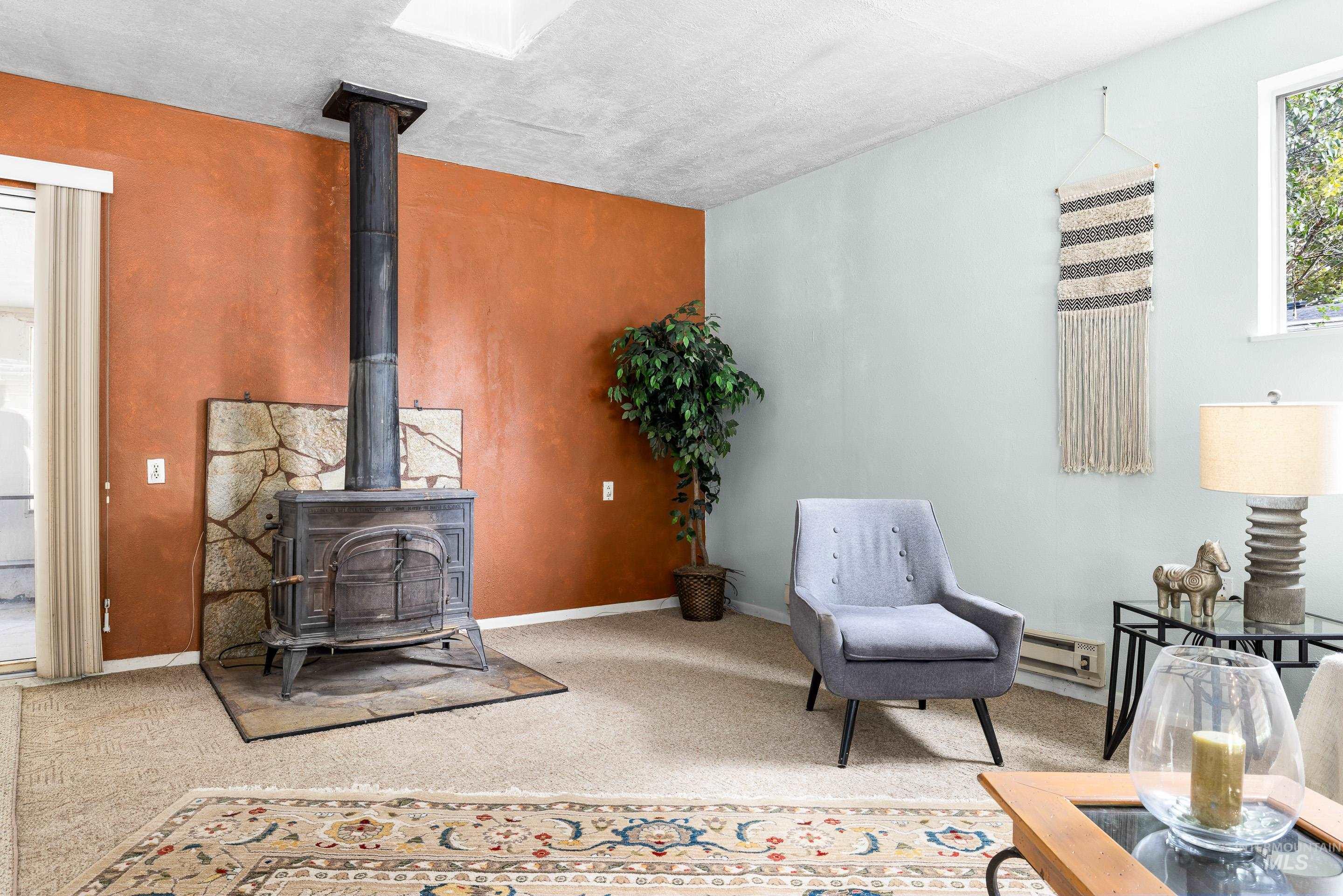 Living area with a wood stove, carpet floors, and a baseboard heating unit