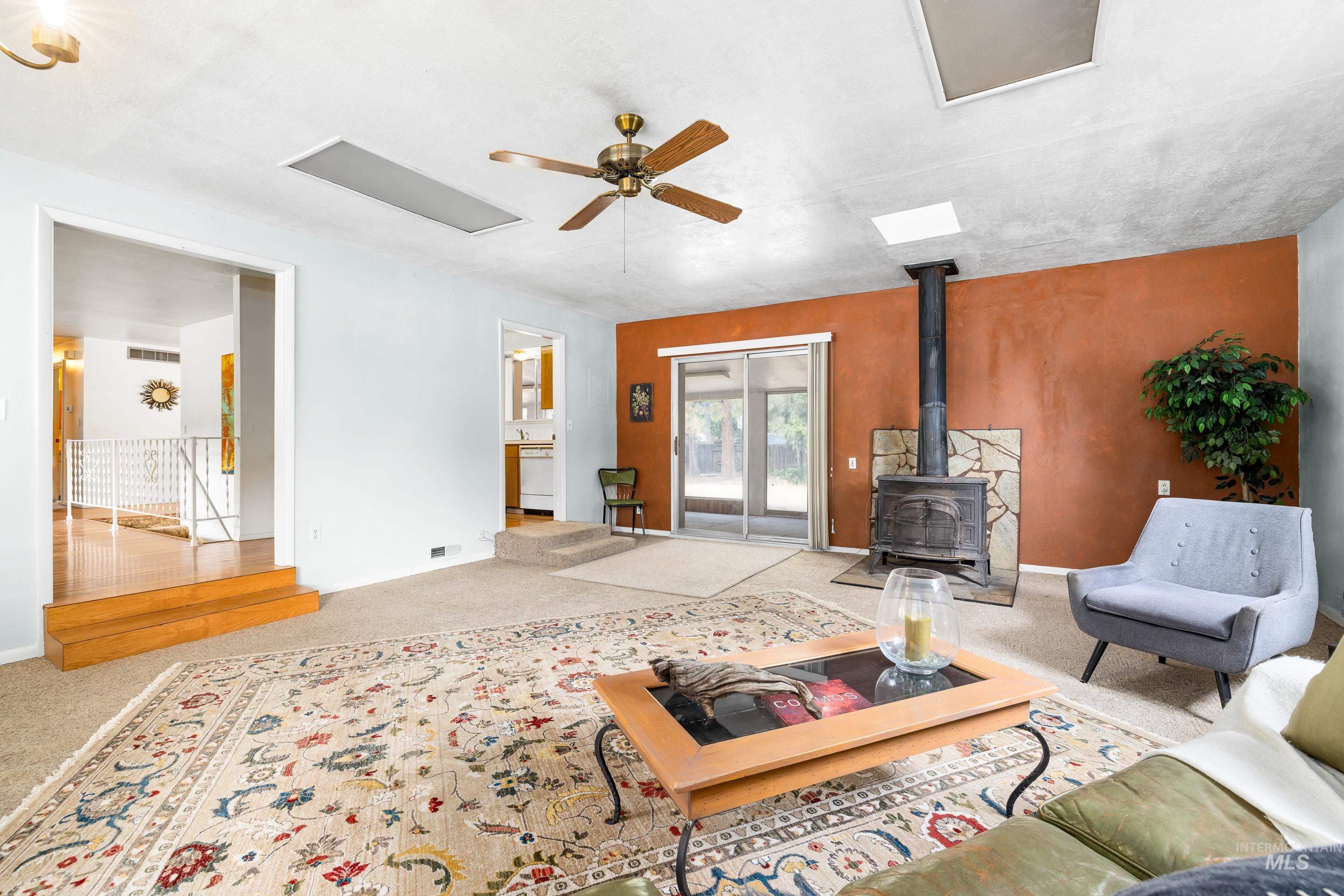 Living area featuring a wood stove, ceiling fan, and carpet floors