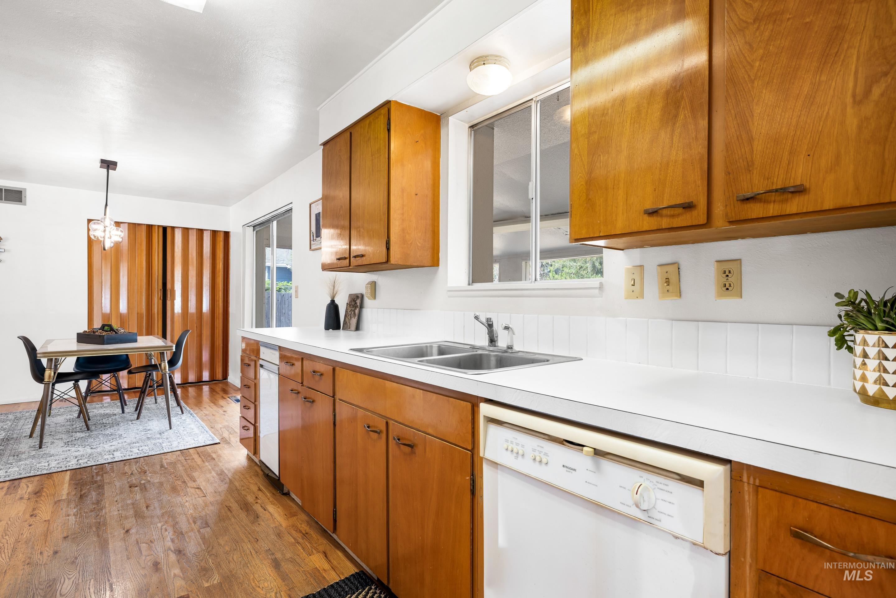 Kitchen with brown cabinetry, white dishwasher, light countertops, and decorative light fixtures