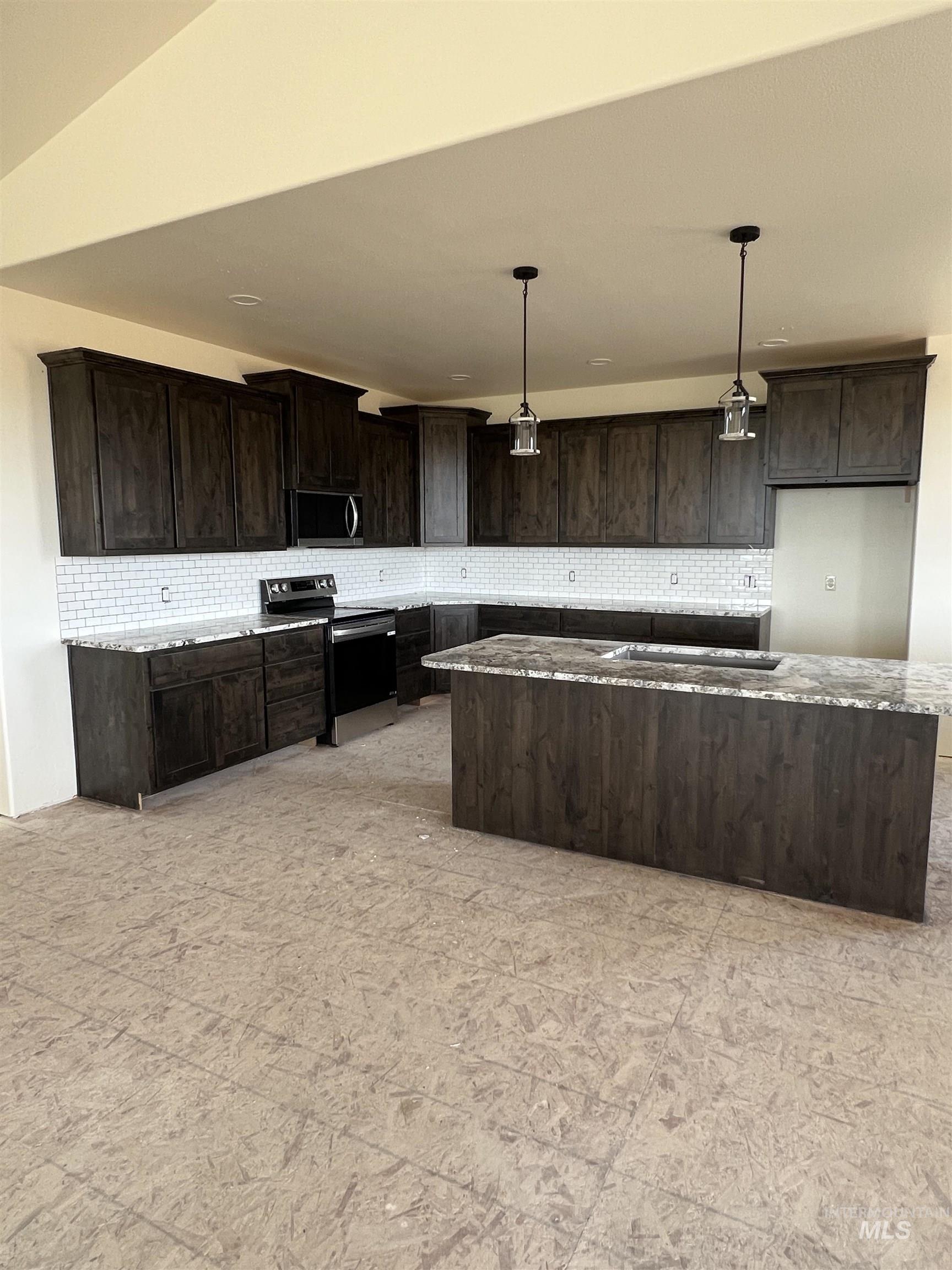 Kitchen featuring tasteful backsplash, dark brown cabinets, appliances with stainless steel finishes, decorative light fixtures, and light stone countertops
