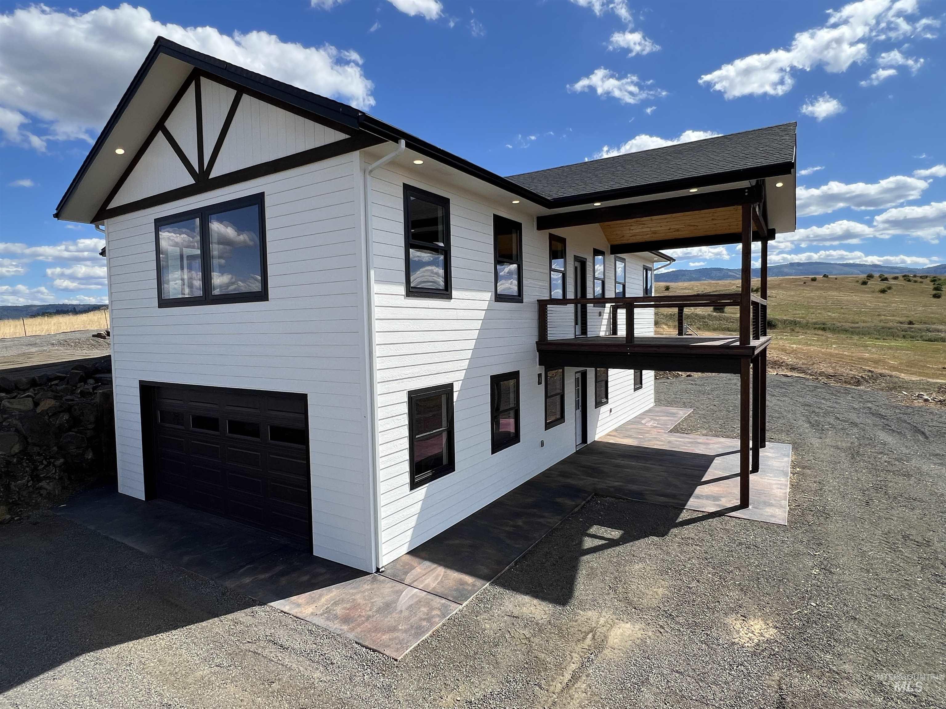 View of property exterior with an attached garage, a balcony, a patio, a shingled roof, and driveway
