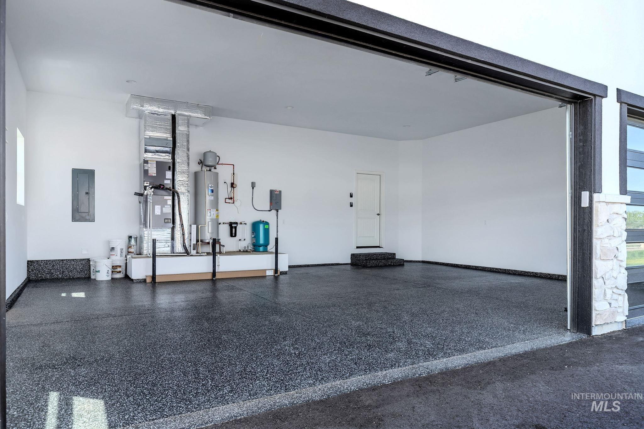 Garage featuring heating unit, electric panel, and electric water heater