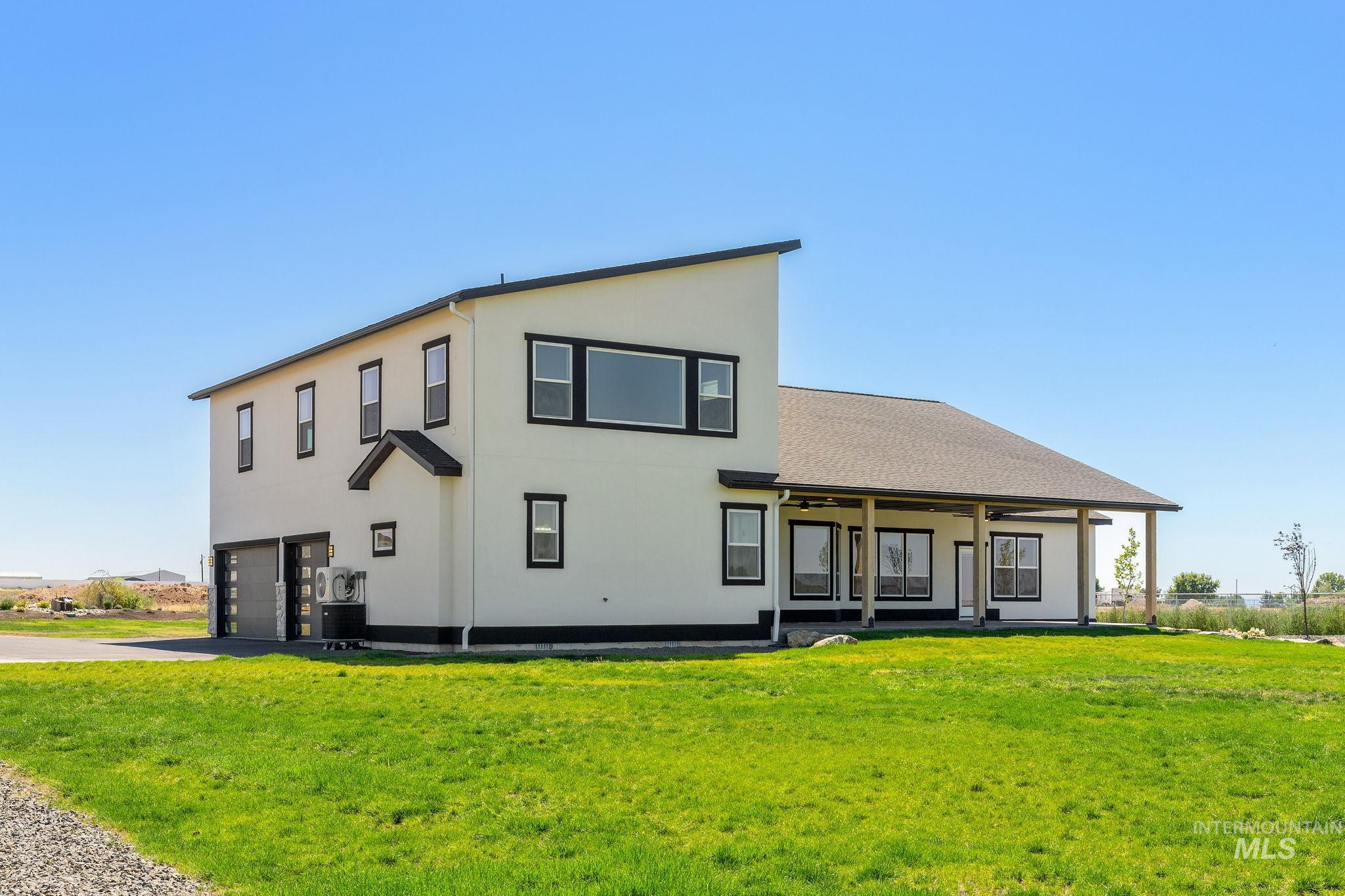 Back of house featuring a garage, stucco siding, a lawn, ceiling fan, and driveway