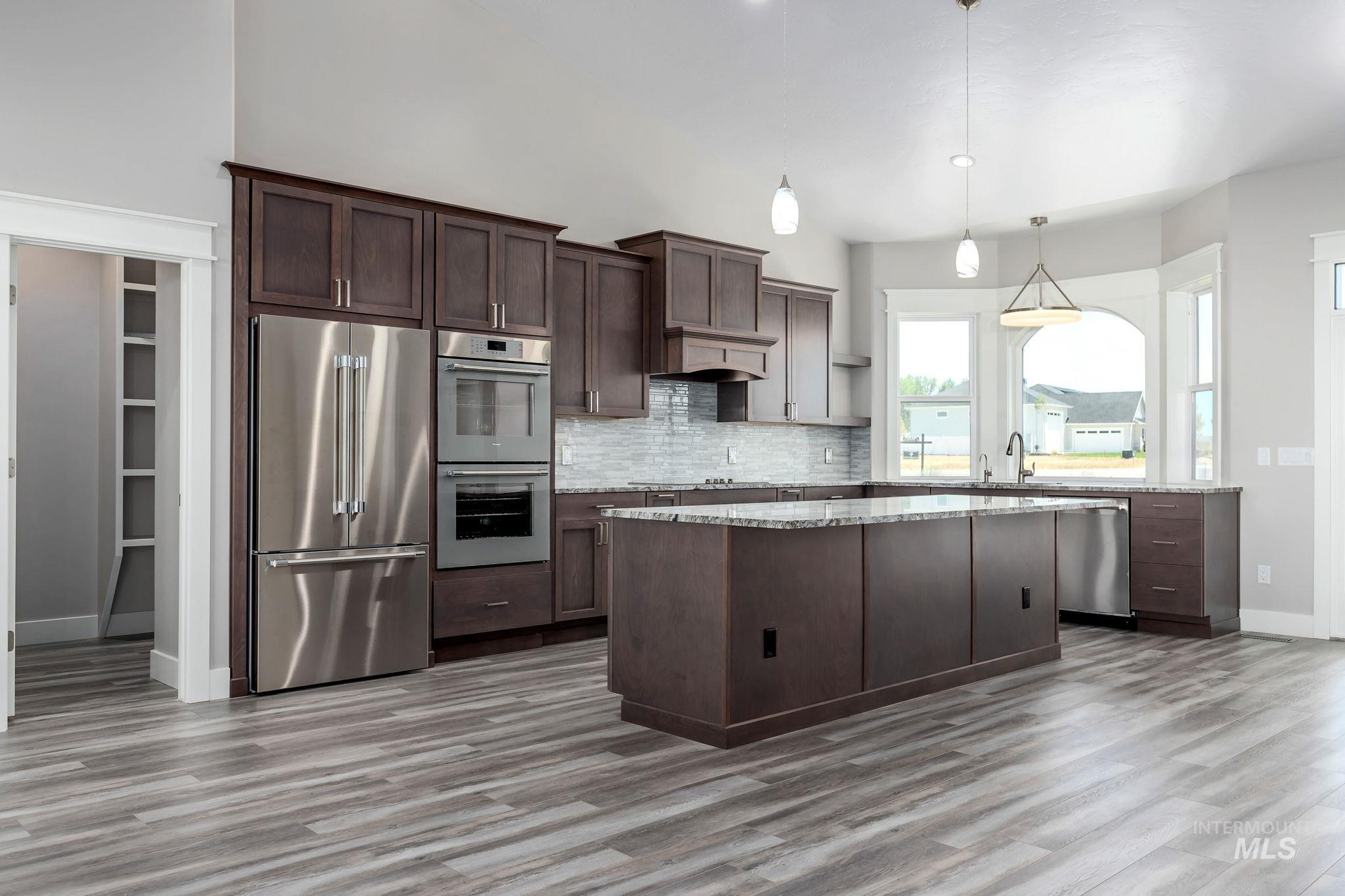 Kitchen with stainless steel appliances, a center island, wood finished floors, decorative backsplash, and dark brown cabinetry