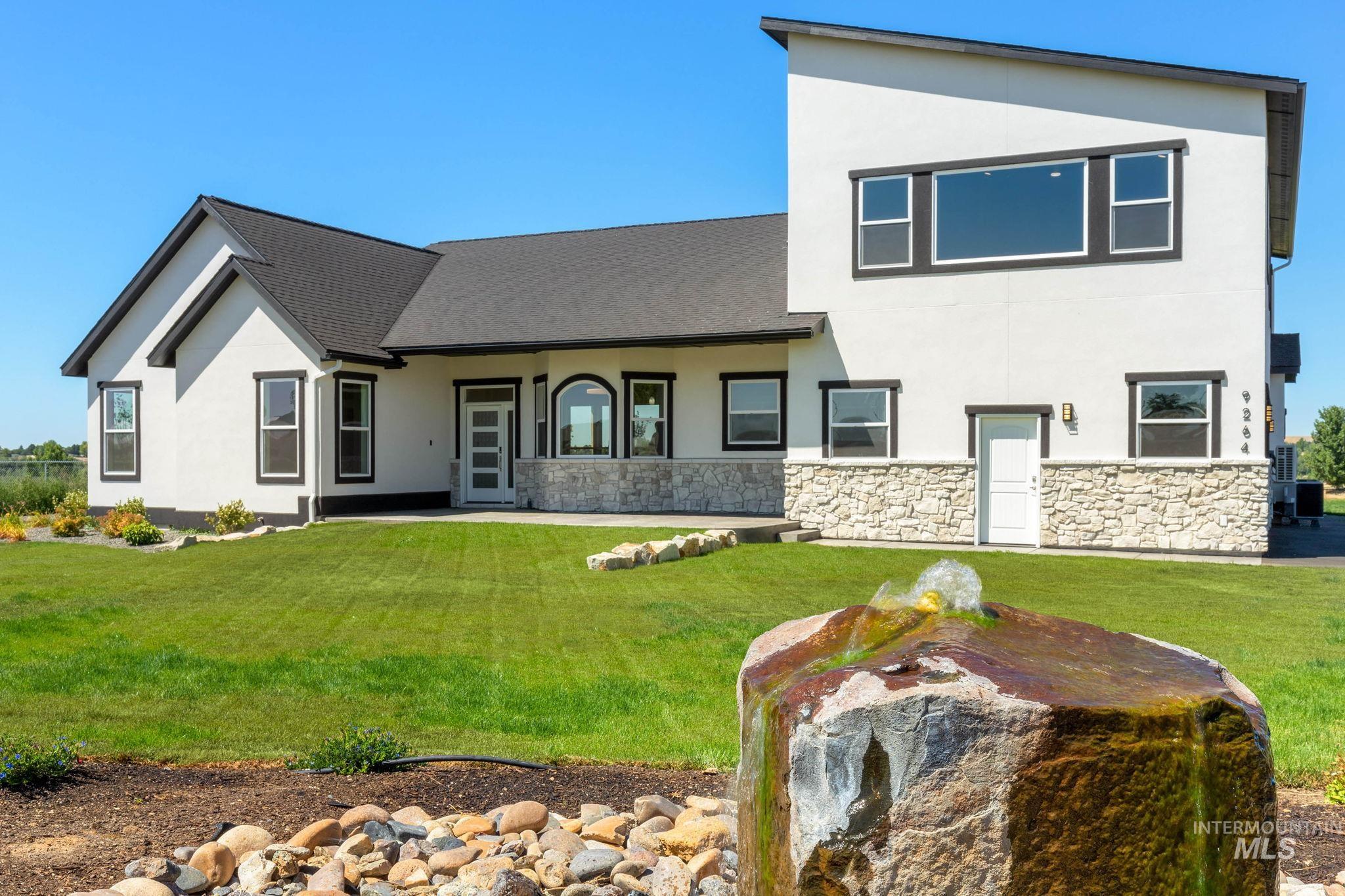 View of front of property with a shingled roof, stucco siding, a front yard, and stone siding